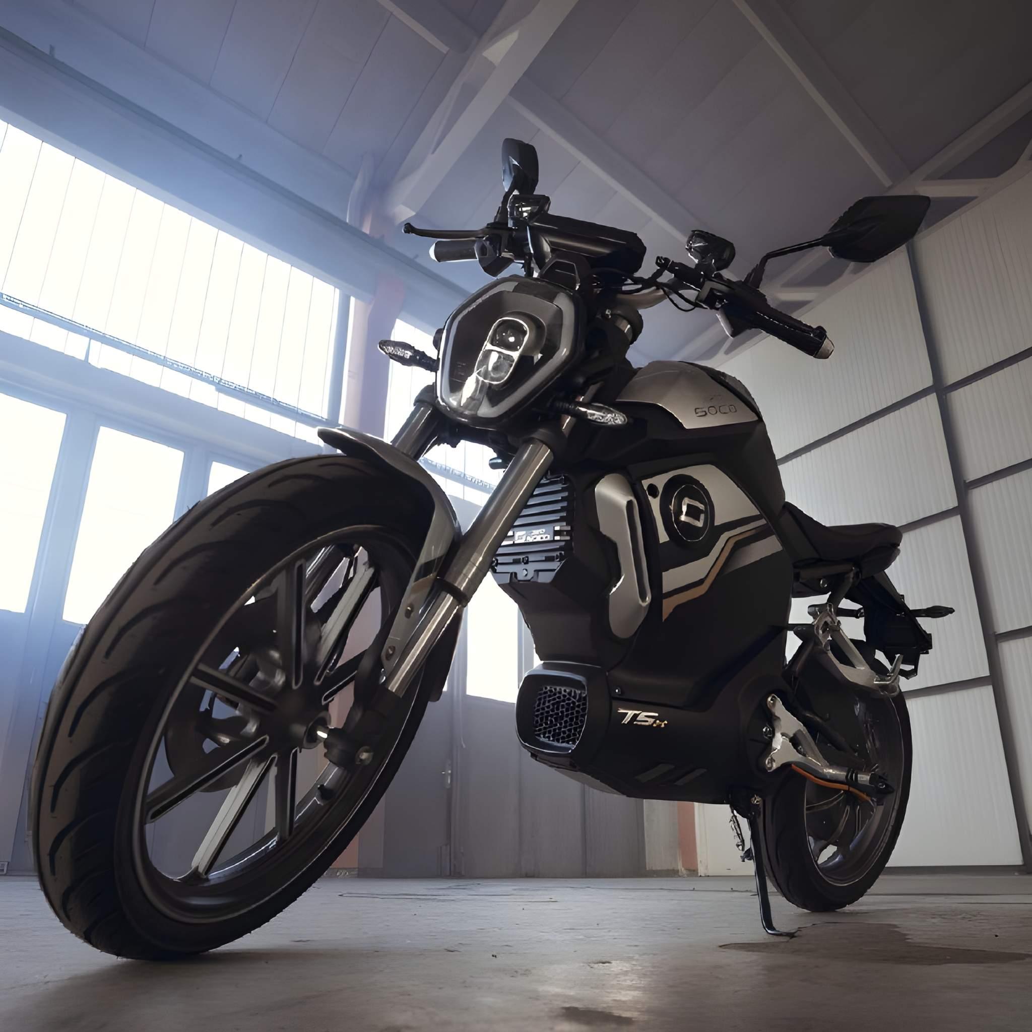 Das Super Soco E-Motorrad TSx Eco 45 km/h mit seinen eleganten schwarzen und silbernen Details steht in einem Innenraum auf einem Betonboden. Ein Blick von unten zeigt die emissionsfreie Leistung und das moderne Vorderraddesign.