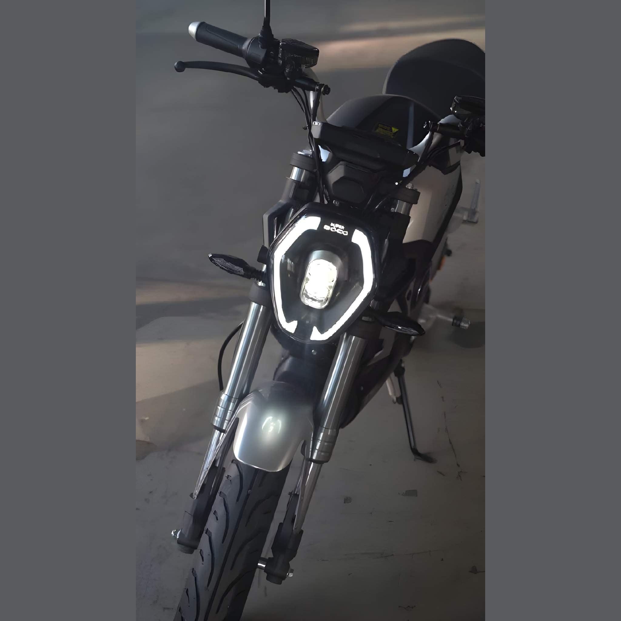Ein schwarzes Super Soco E-Motorrad TSx Eco 45 km/h, von vorne auf einer Betonfläche betrachtet, zeigt seinen Scheinwerfer mit einem sechseckigen LED-Muster. Auch der Lenker und ein Teil des Sitzes sind zu sehen.