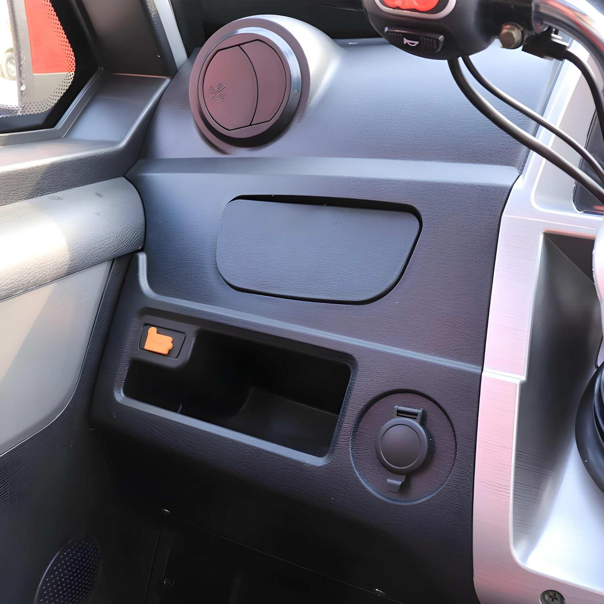 Nahaufnahme des EQ-Mobil Kabinenroller Lima Q3 Li 45 / 25 km/h Armaturenbretts: leeres Staufach, orangefarbene Verriegelung, runde Steckdose, Lüftungsöffnung an der Windschutzscheibe und Lenkradgriff - ideale Stadtmobilität mit Lithium-Akku.