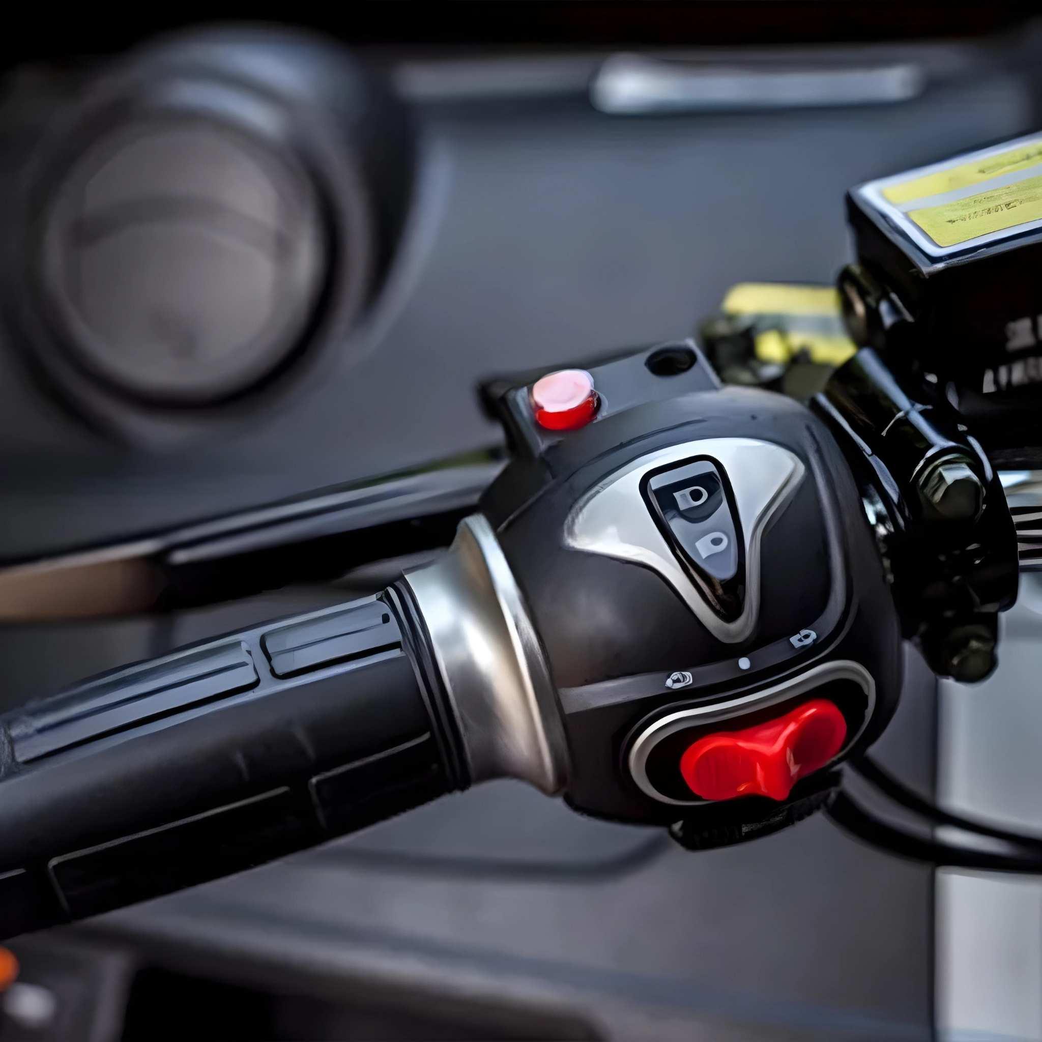 Nahaufnahme eines schwarzen Lenkergriffs mit Knöpfen, darunter ein roter Knopf, ein D/P-Kippschalter und herzförmige Bedienelemente des EQ-Mobil Kabinenrollers Lima Q3 Li 45 / 25 km/h (Lithium Akku), vor einem unscharfen Hintergrund.