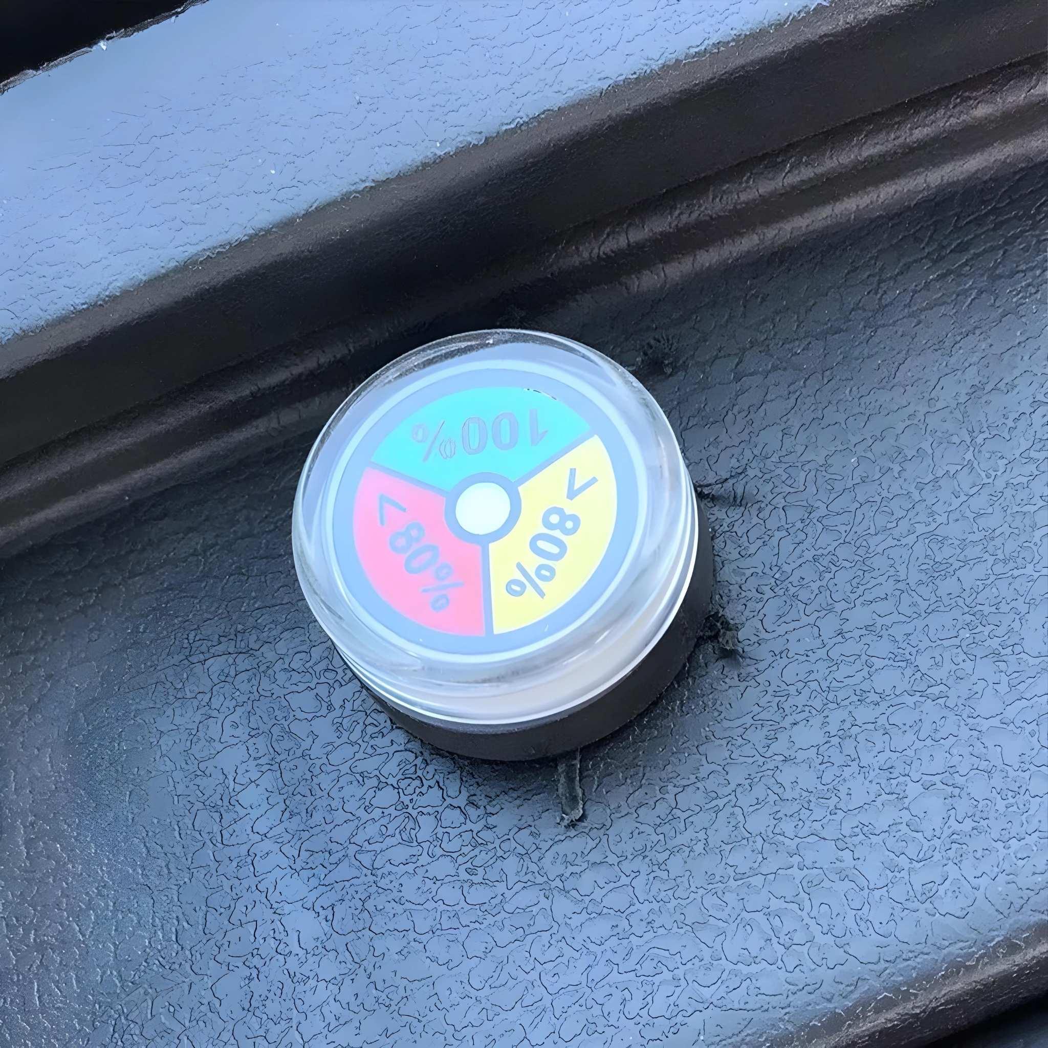 Der kompakte runde Behälter von EQ-Mobil, der für den Kabinenroller Lima Q3 Li 45 / 25 km/h konzipiert wurde, verfügt über einen Deckel mit farblich gekennzeichneter Anzeige (<80%, 80%, 100% in gelb, rot, grün, blau) und ruht auf einer strukturierten schwarzen Oberfläche.