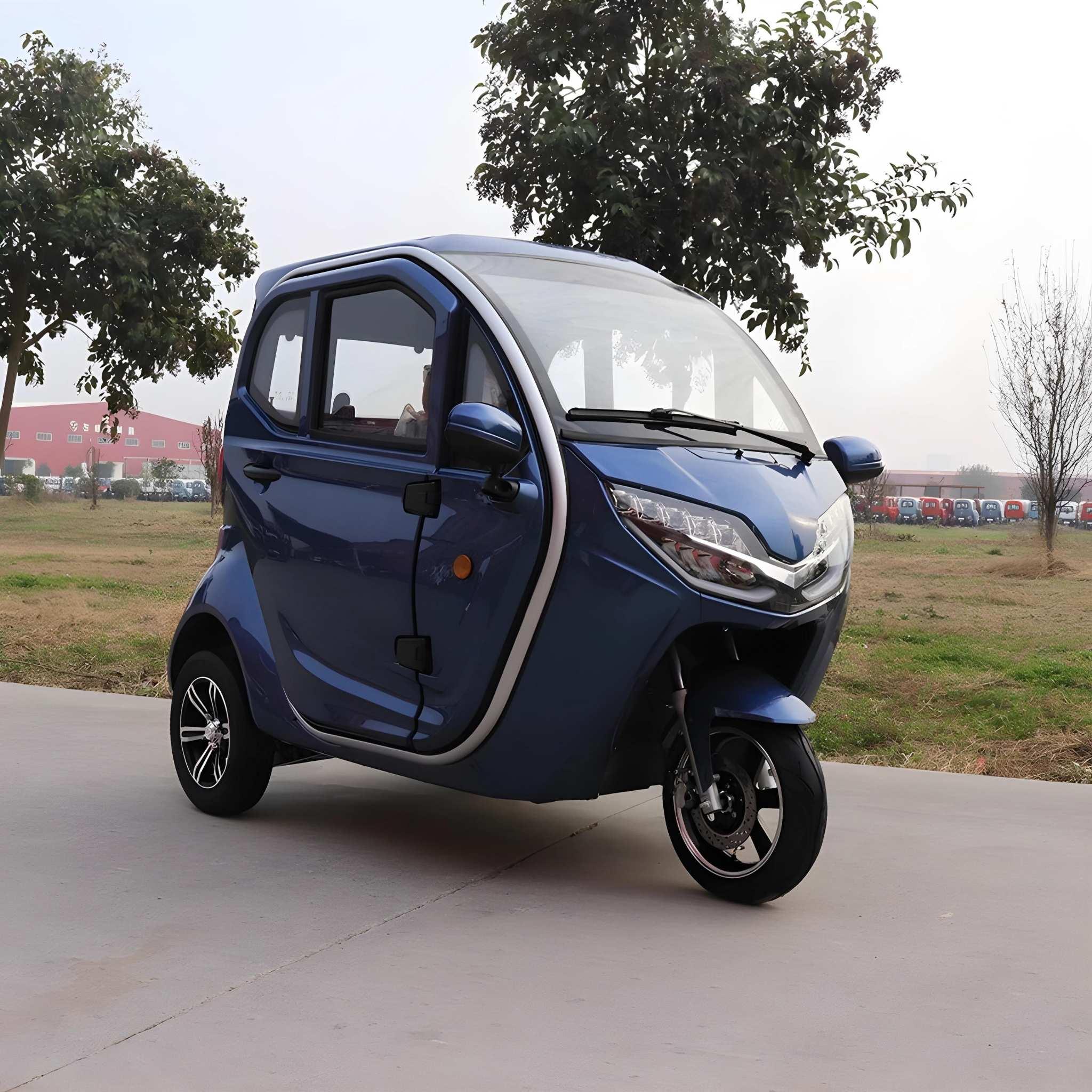 Ein EQ-Mobil Kabinenroller Lima Q3 Li 45/25 km/h mit Lithium-Akku, ein kompaktes blaues dreirädriges geschlossenes Elektrofahrzeug, ist auf einem gepflasterten Weg mit Bäumen und einer Wiese im Hintergrund geparkt.