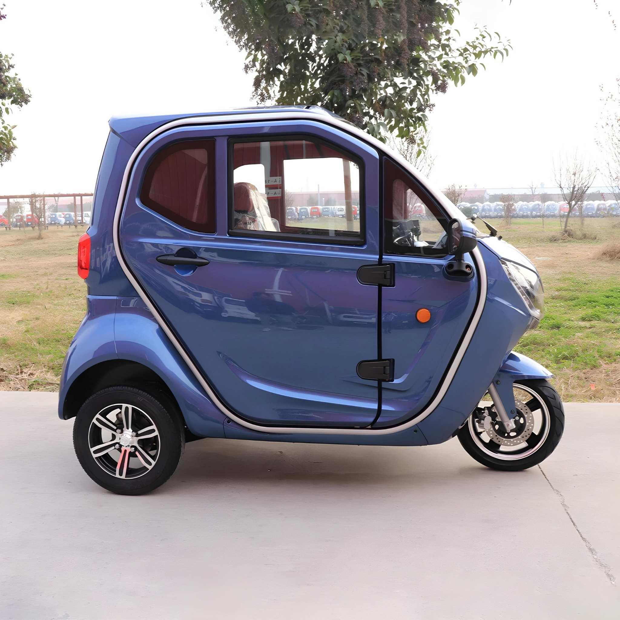 Ein kompakter, blauer EQ-Mobil Kabinenroller Lima Q3 Li 45/25 km/h mit Lithium-Batterie steht im Freien auf dem Bürgersteig, umgeben von Gras, Bäumen und einem Parkplatz im Hintergrund.