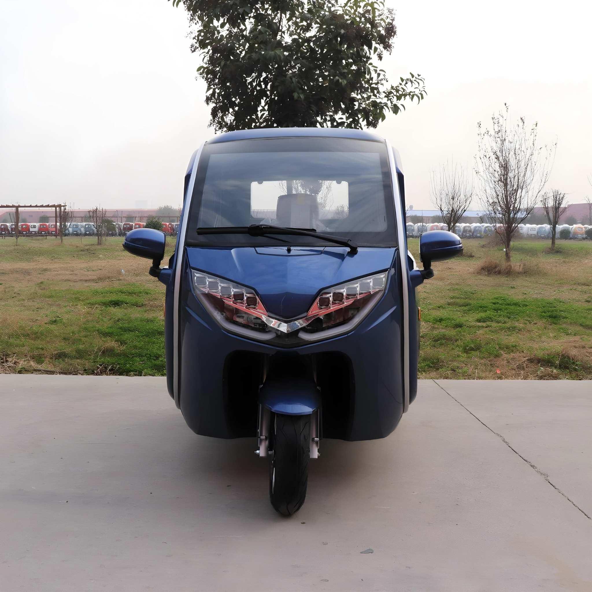 Ein blauer EQ-Mobil Kabinenroller Lima Q3 Li 45/25 km/h, aktuelles Modell mit Lithium-Akku, ist auf einer Betonfläche mit Blick auf die Kamera geparkt, mit Grasflächen und Bäumen im Hintergrund.
