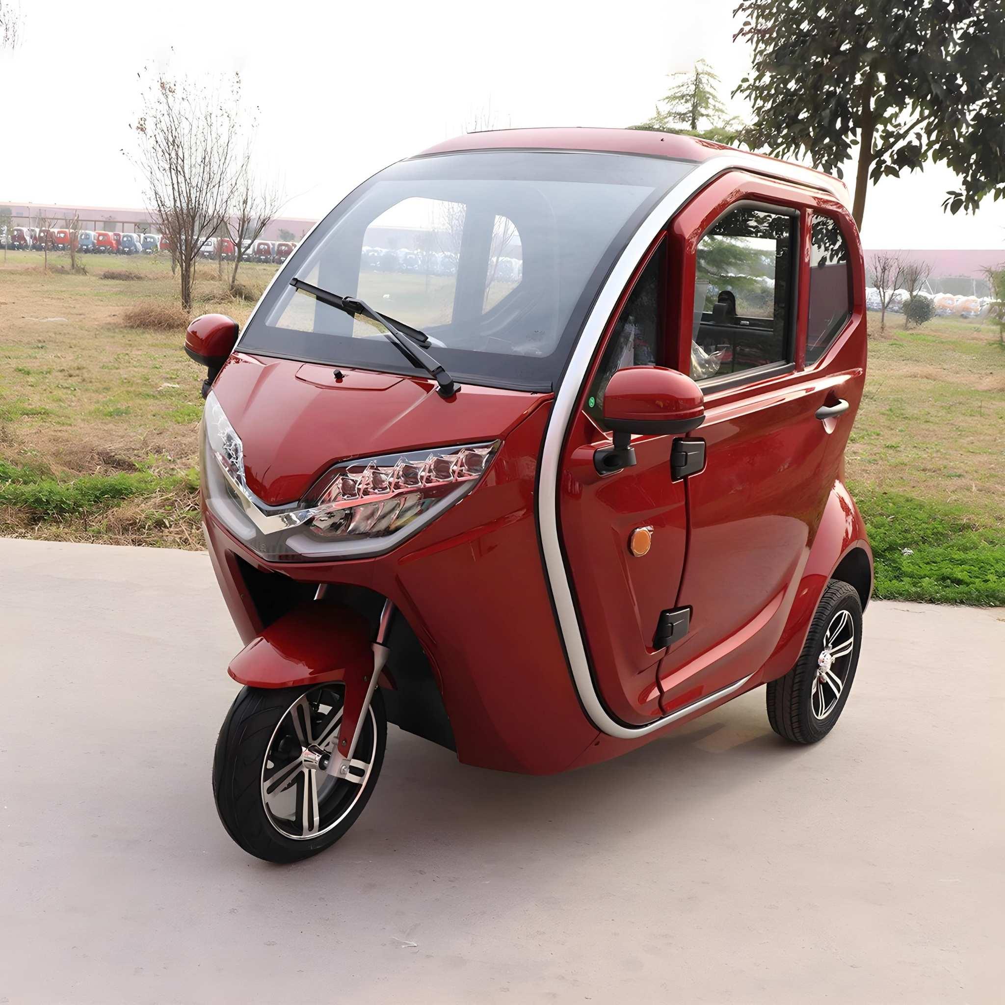 Ein kompakter, roter EQ-Mobil Kabinenroller Lima Q3 Li 45 / 25 km/h mit Lithium-Akku steht auf einer gepflasterten Fläche inmitten von Gras und Bäumen, in der Ferne ist eine Reihe von Autos zu sehen.