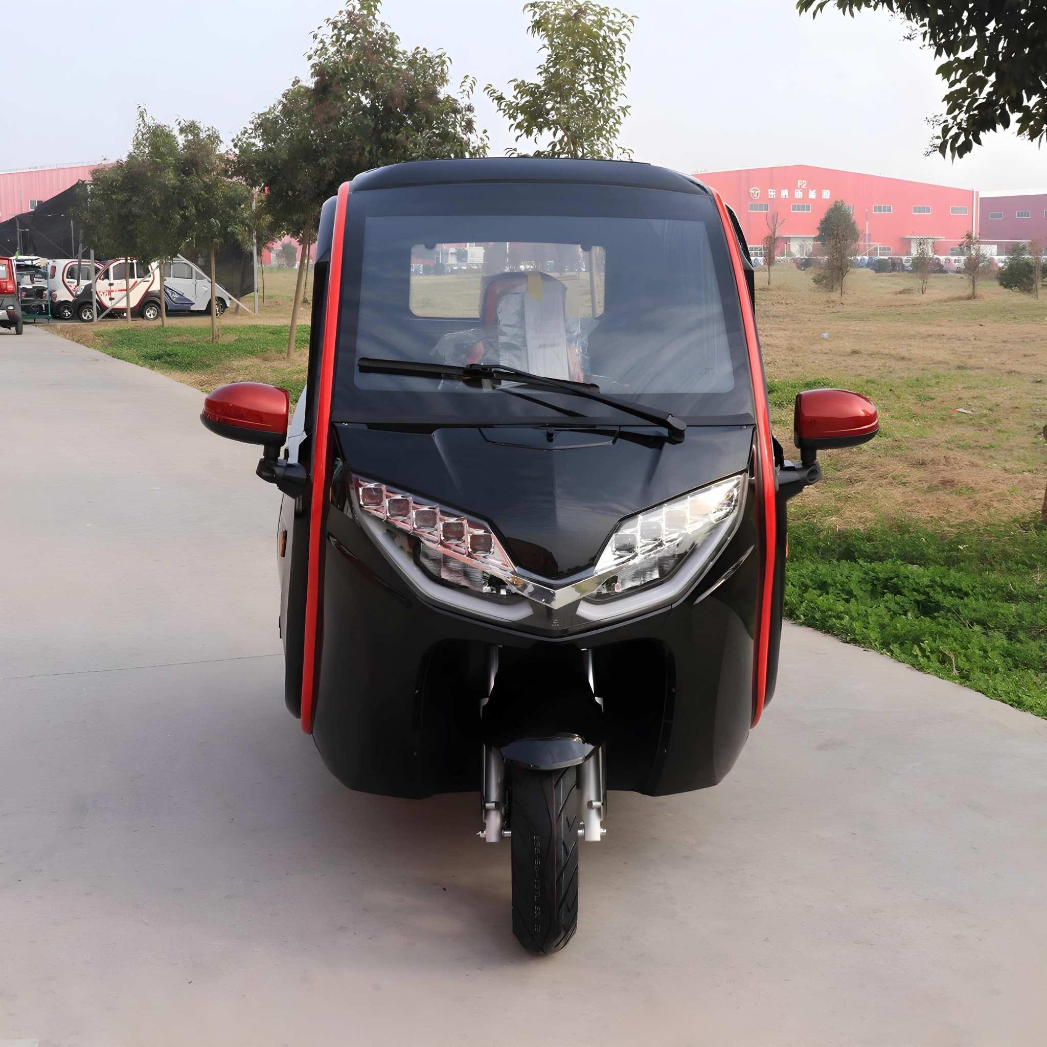 Ein schwarzer EQ-Mobil Kabinenroller Lima Q3 Li 45 mit roten Akzenten, der von einer Lithiumbatterie angetrieben wird, parkt auf einer gepflasterten Straße, die von Gras und Bäumen gesäumt ist, mit roten Gebäuden im Hintergrund.