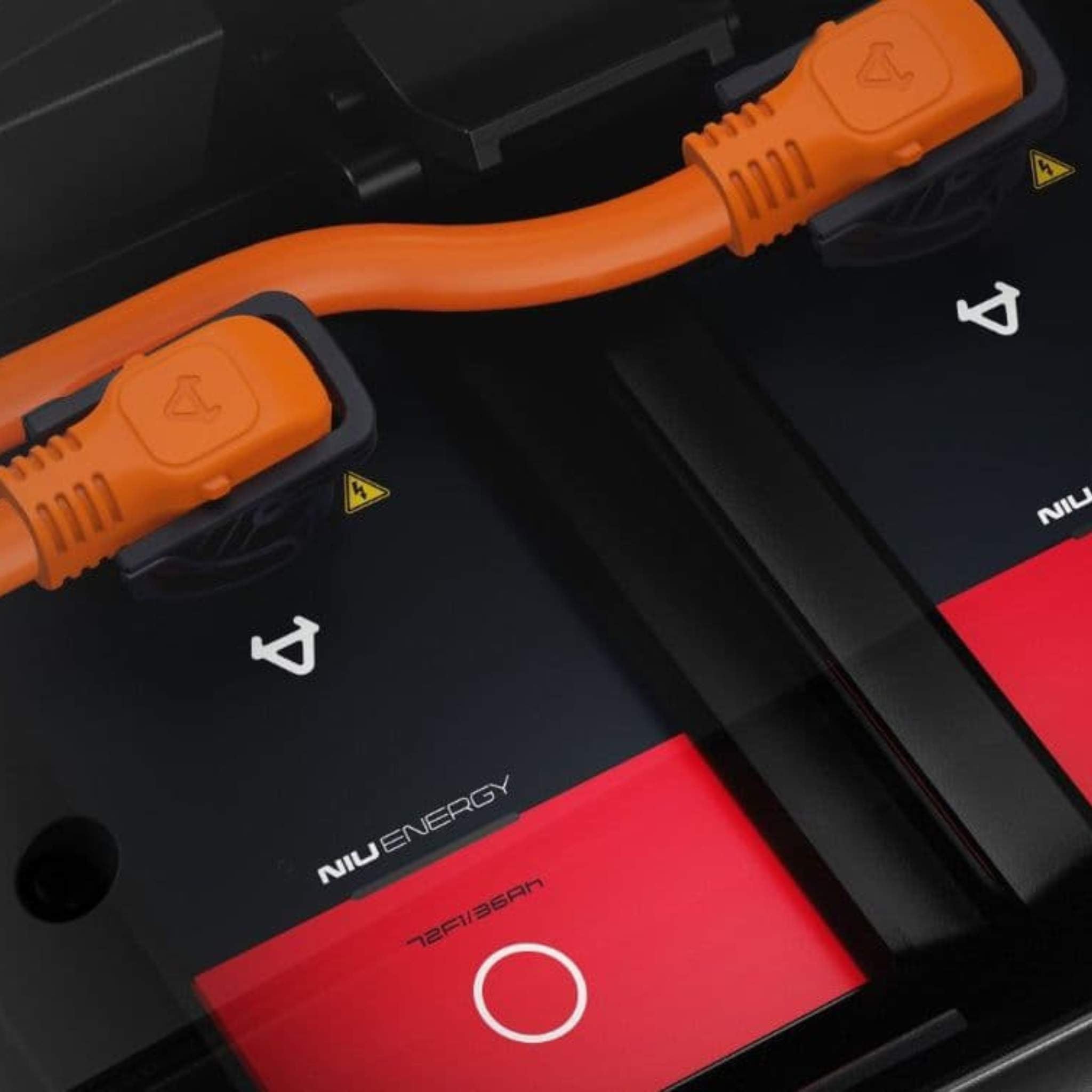 Nahaufnahme von zwei orangefarbenen Stromanschlüssen, die in schwarze und rote NIU-Akkus mit Warnsymbolen eingesteckt sind, wie sie am Elektromotorrad NIU RQI Sport 110 km/h - ideal für dieses moderne NIU-E-Motorrad - zu sehen sind.