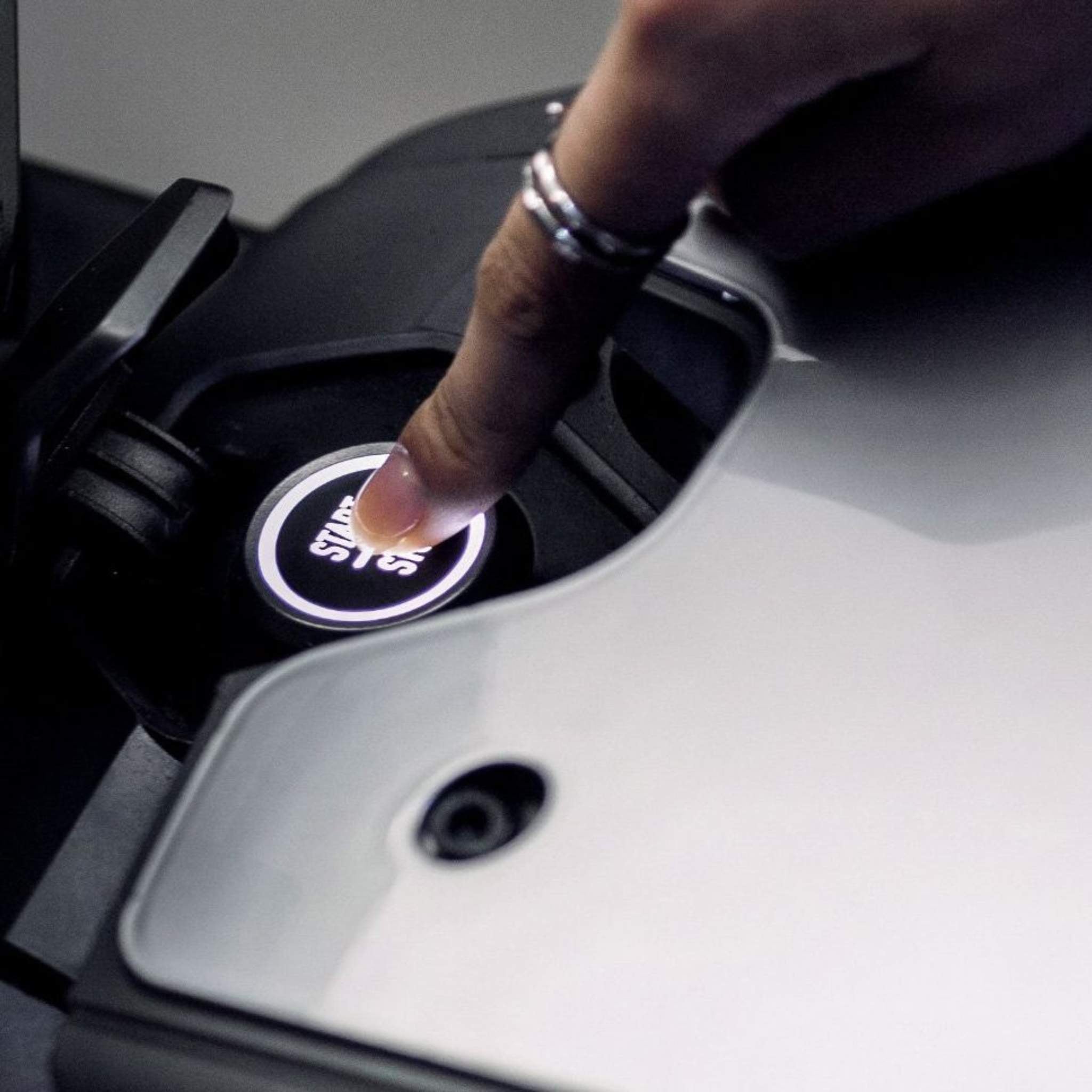 Eine Nahaufnahme zeigt eine Person mit zwei silbernen Ringen, die einen beleuchteten Knopf mit asiatischen Schriftzeichen drückt, wahrscheinlich um das NIU Elektromotorrad RQI Sport 110 km/h zu starten.