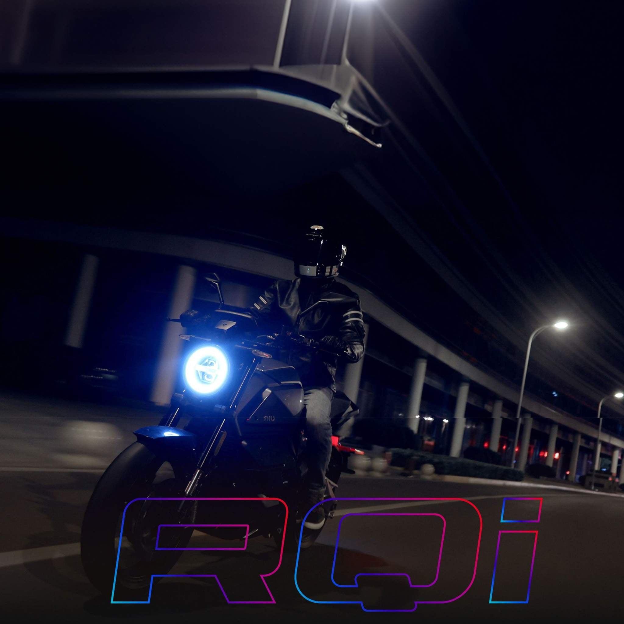 Eine Person mit Helm und dunkler Kleidung fährt auf einem NIU Elektromotorrad RQI Sport (110 km/h) mit einem leuchtenden runden Scheinwerfer bei Nacht auf einer Stadtstraße. Der fette, bunte Schriftzug "RQI" ist am unteren Rand überlagert. Marke: NIU.