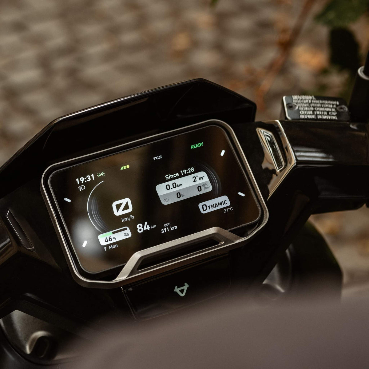 Nahaufnahme des digitalen Armaturenbretts eines NIU NQiX 500 Elektrorollers (Modell 2025) von NIU, auf dem Geschwindigkeit, Fahrdaten, Akkustatus, Temperatur und Fahrmodi angezeigt werden. Im Hintergrund ist eine unscharf abgebildete Straßenoberfläche im Freien zu sehen.