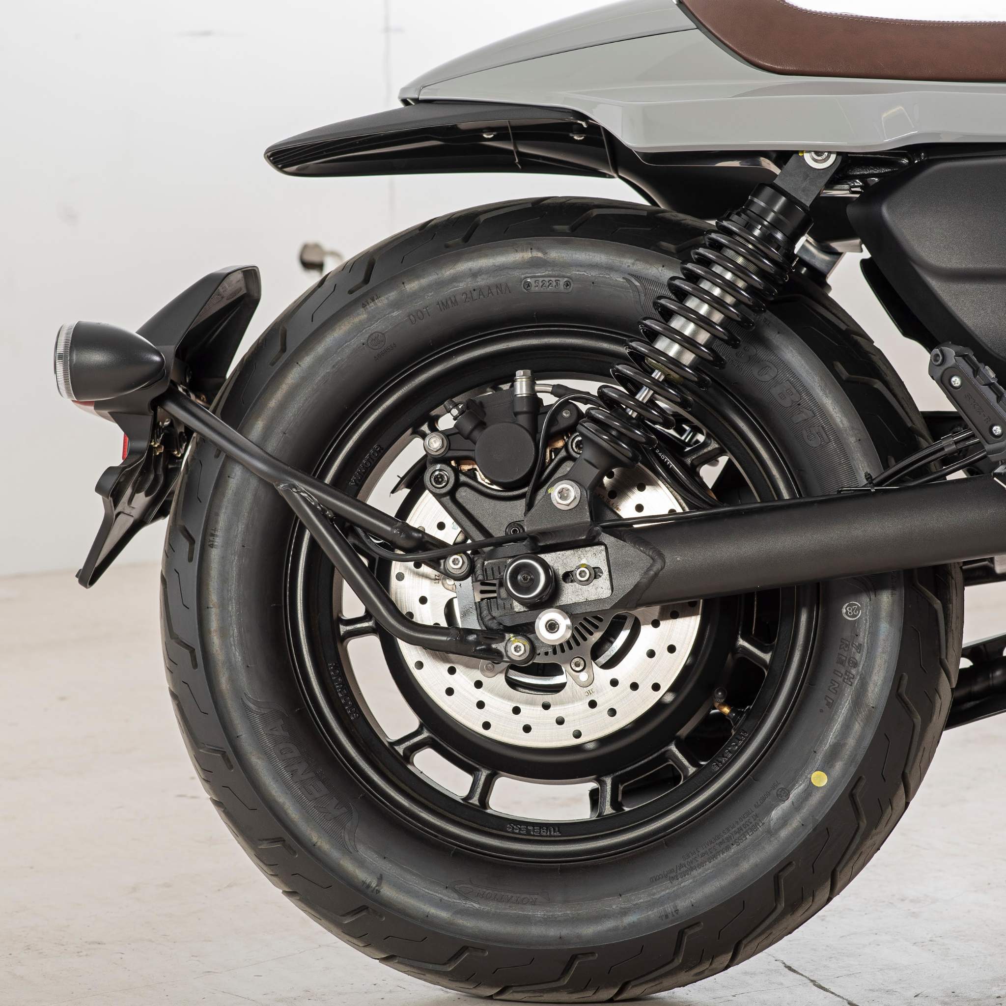 Nahaufnahme des Hinterrads des E.F.O. Elektro Motorrad EM8 120 km/h - Aktionspreis! mit Reifen, Scheibenbremse, Tragfeder und Schutzblech vor einem schlichten Hintergrund, der Innovation und Umweltprämie hervorhebt.