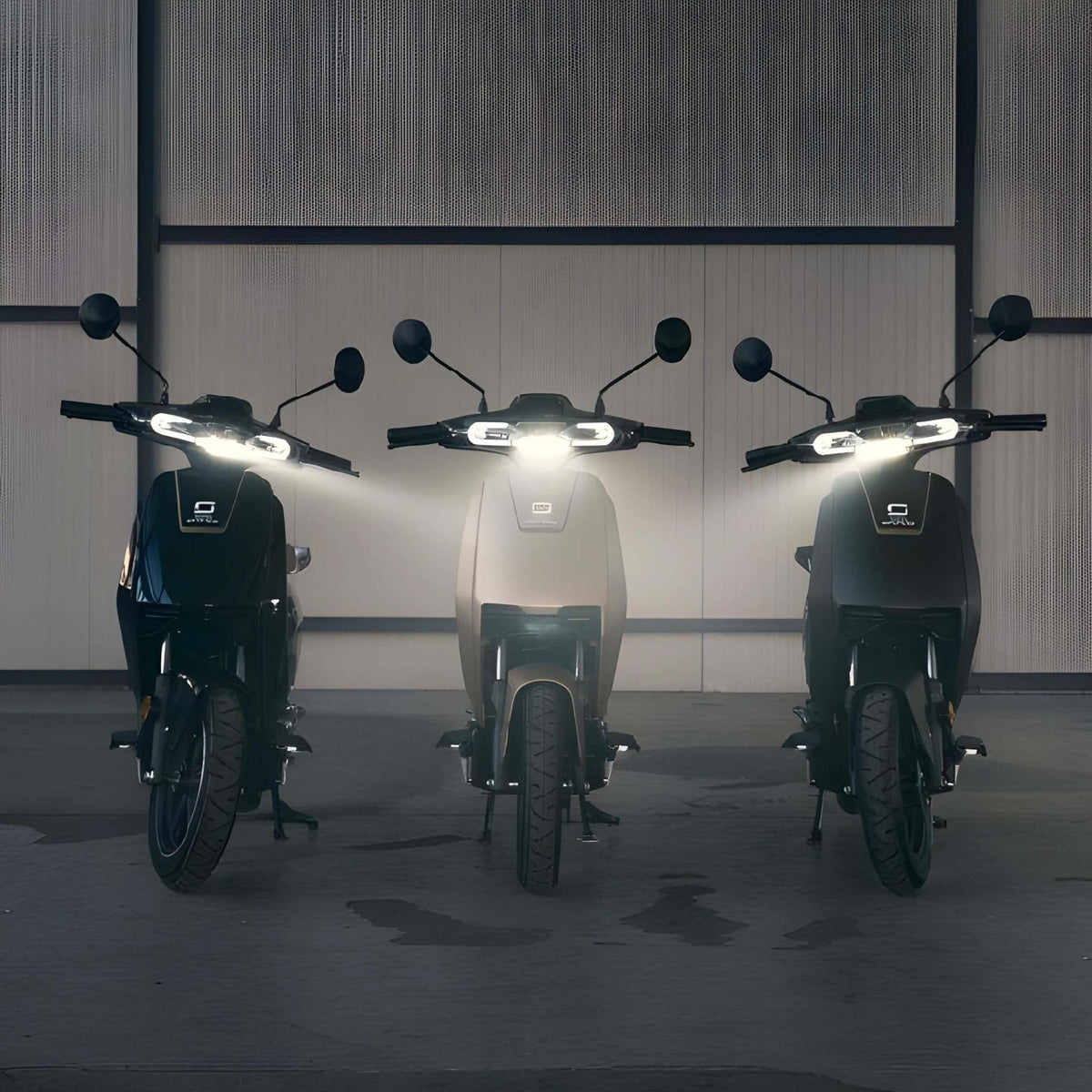 Drei Super Soco Elektroroller CUx Pro mit eingeschalteten Scheinwerfern stehen in einer Halle nebeneinander an einer Metallwand und präsentieren den leichten 45 km/h E-Roller mit Bosch-Power und umweltfreundlicher Mobilität.