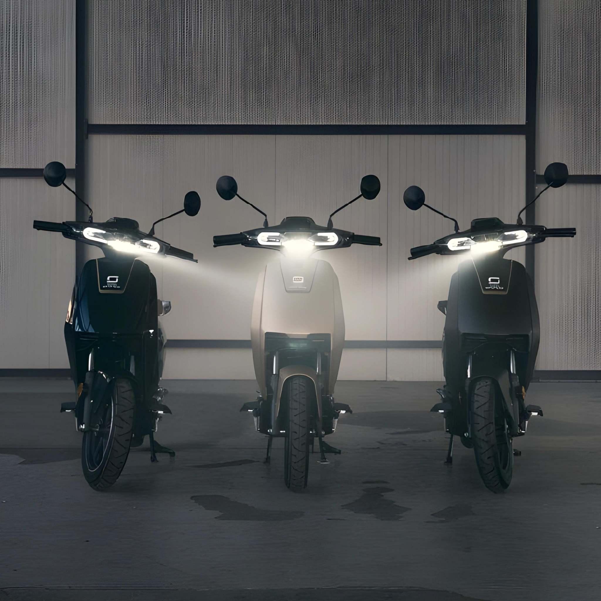 Drei Super Soco Elektroroller CUx Pro mit eingeschalteten Scheinwerfern stehen in einer Halle nebeneinander an einer Metallwand und präsentieren den leichten 45 km/h E-Roller mit Bosch-Power und umweltfreundlicher Mobilität.