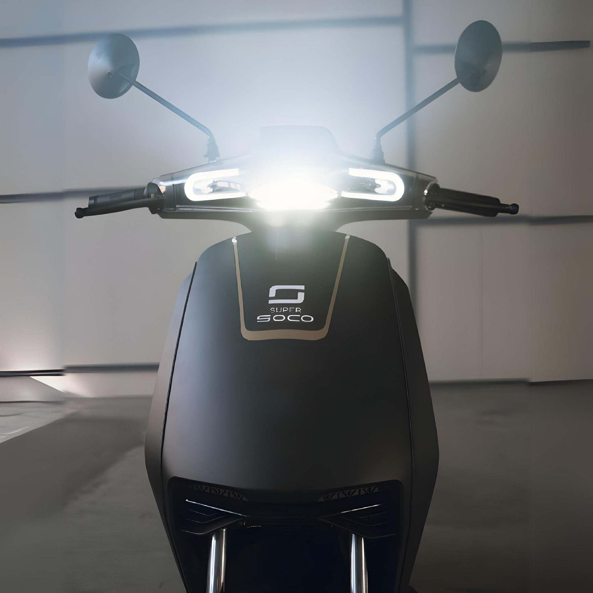 Frontansicht des Super Soco CUx Pro Elektrorollers, eines 45 km/h leichten E-Scooters mit Bosch-Power, mattschwarzer Karosserie und eingeschaltetem Scheinwerfer - ideal für umweltfreundliche Mobilität - vor einem unscharfen Indoor-Hintergrund.