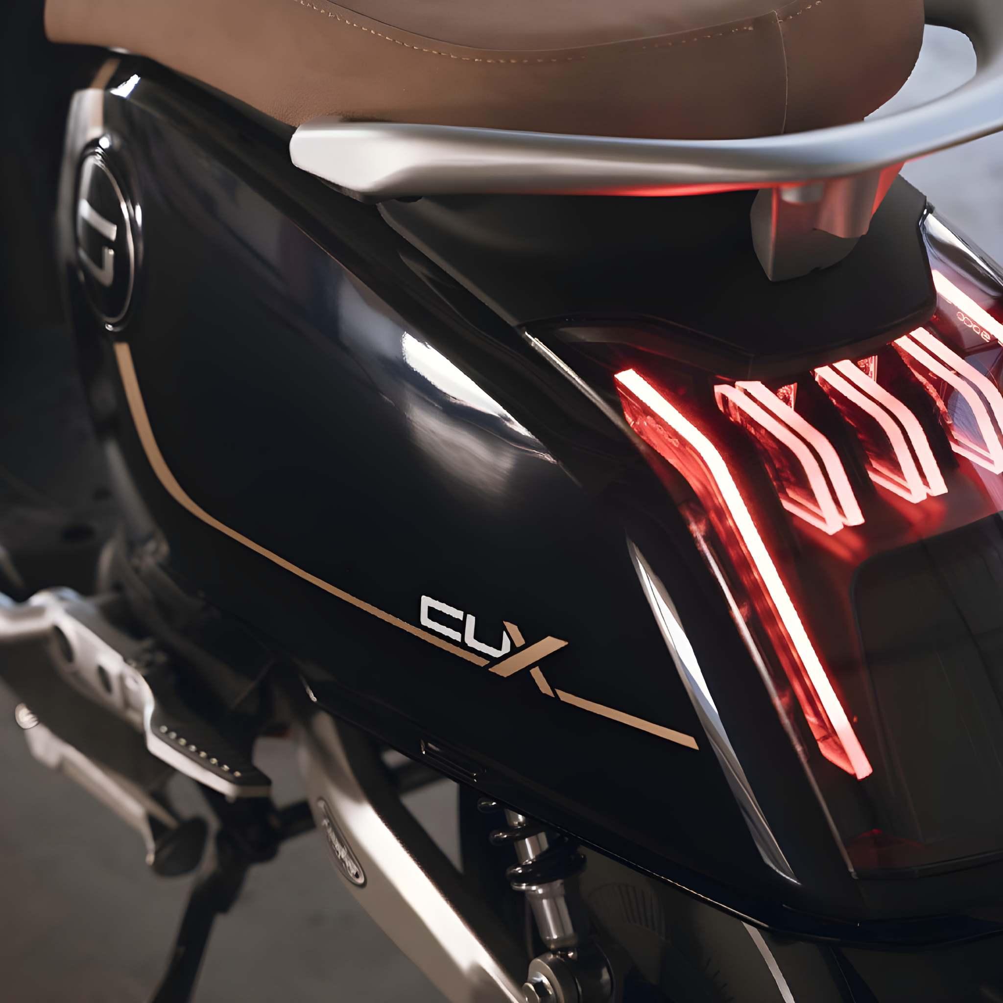 Nahaufnahme des Super Soco CUx Pro Elektrorollers: Schwarzes Design, braune Sitzbank, silberner Haltegriff und leuchtend rote LED-Rückleuchten - umweltfreundliche Mobilität in stylischer 45-km/h-Bosch-Form.