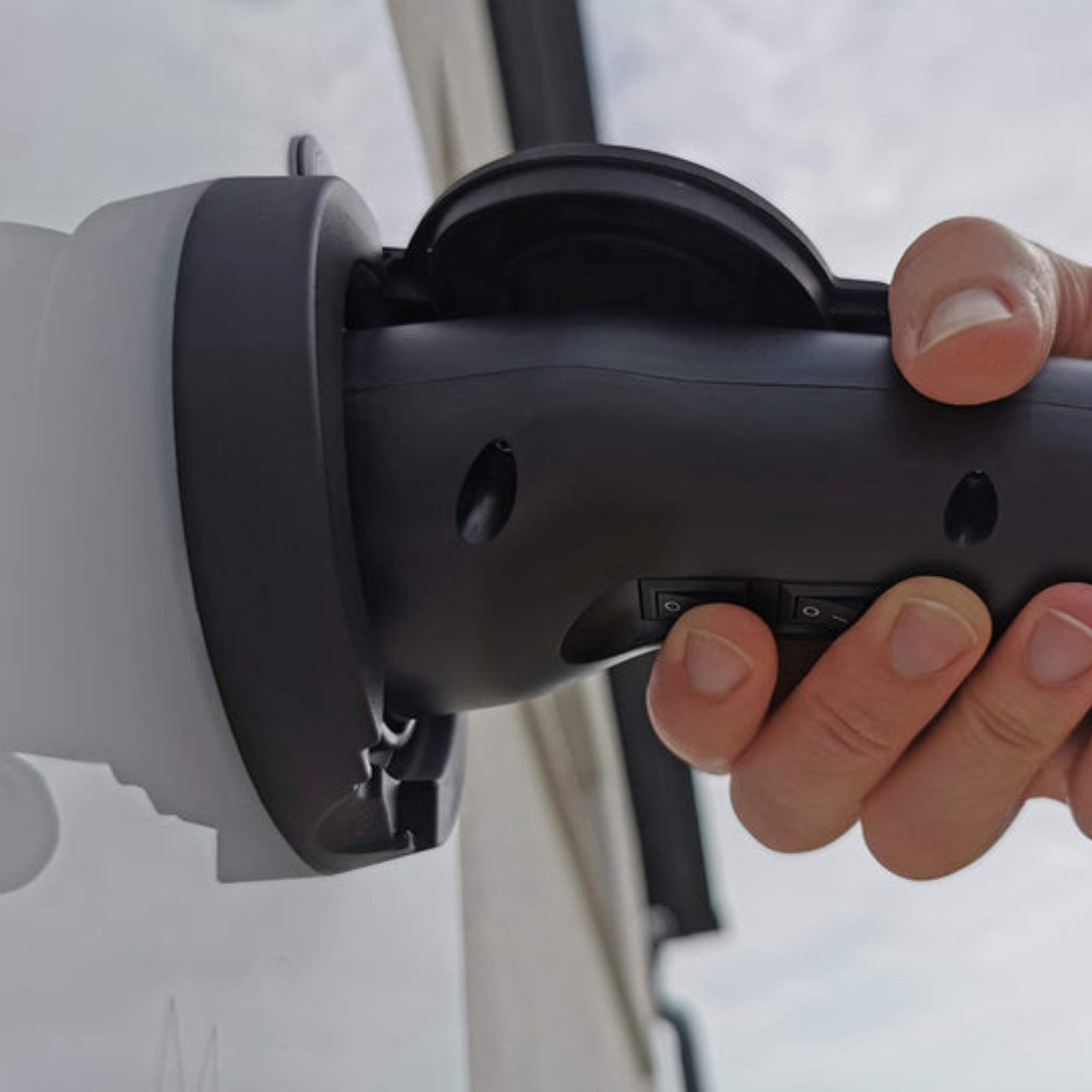 Eine Hand steckt einen VMOTO TYP2 Adapter für Schuko Stecker in einen E-Roller an einer Ladestation, Gebäude und Himmel verschwimmen im Hintergrund - die zuverlässige Ladelösung für dein Elektro Motorrad, E-Chopper, Roller & Scooter!.