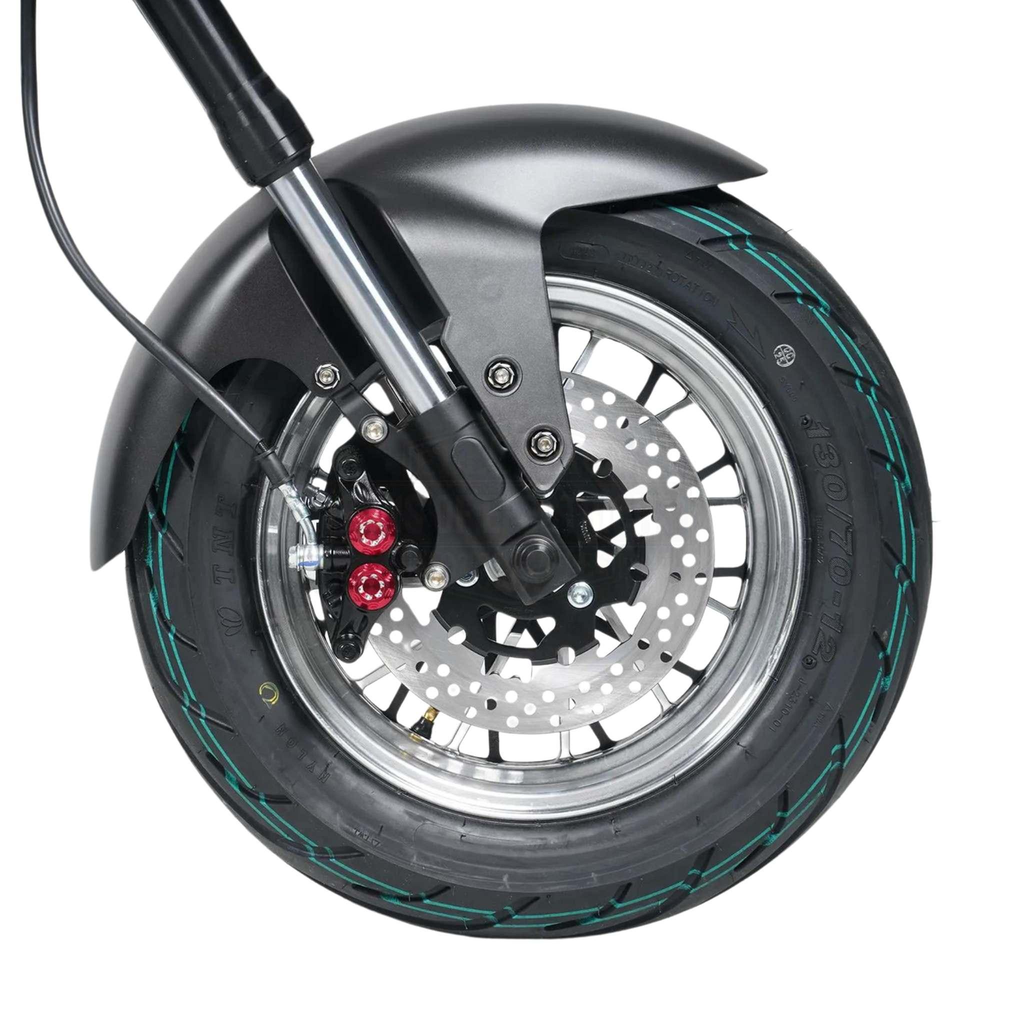 Nahaufnahme des Vorderrads des Mangosteen E-Chopper M1P mit einem schwarzen Reifen mit grünen Streifen, silberner Scheibenbremse, schwarzem Schutzblech und Federgabel.