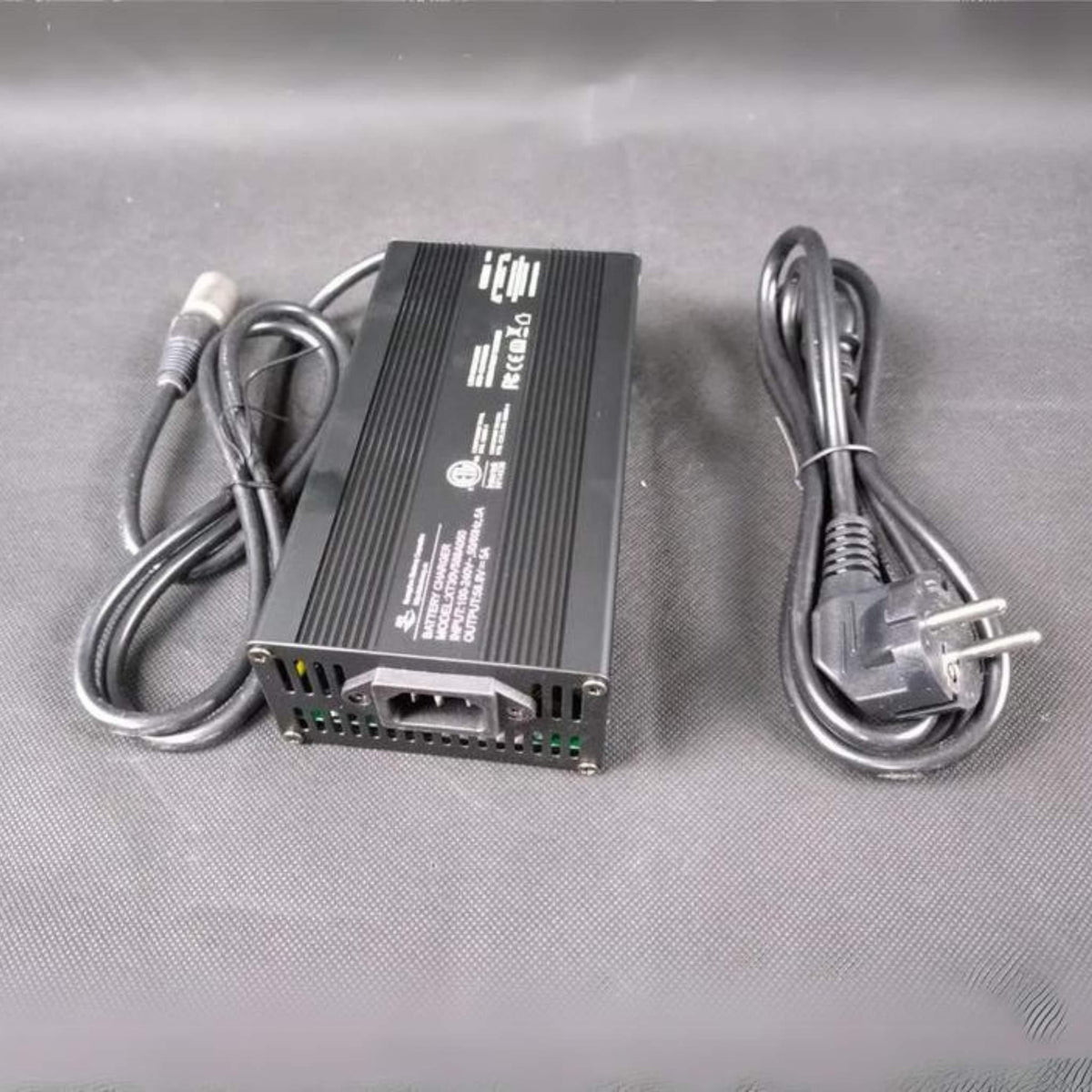 Ein Wandler WANDLER L/E, K/E eScooter Schnellladegerät 5A für 52V Lithium-Batterie liegt auf einer dunklen Stofffläche mit den daran befestigten Kabeln und einem separaten schwarzen zweipoligen Netzkabel in der Nähe.