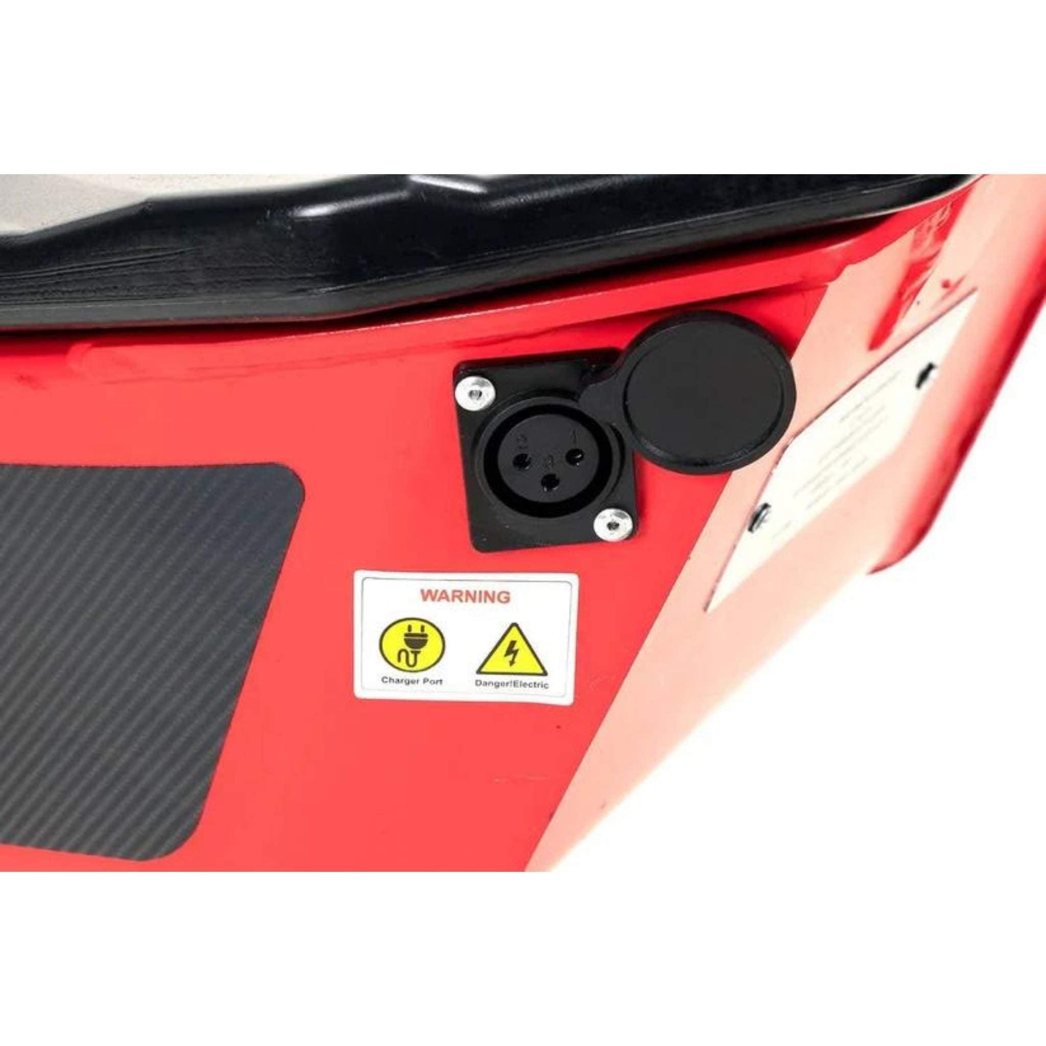 Nahaufnahme des roten Wandler E-Rollers/E-Scooters K/E 45 km/h 2025, wobei der schwarze kreisförmige Ladeanschluss mit Klappdeckel neben einem Warnschild mit Symbolen für elektrische Gefahren und "Charge Port" und "Danger: Electric".