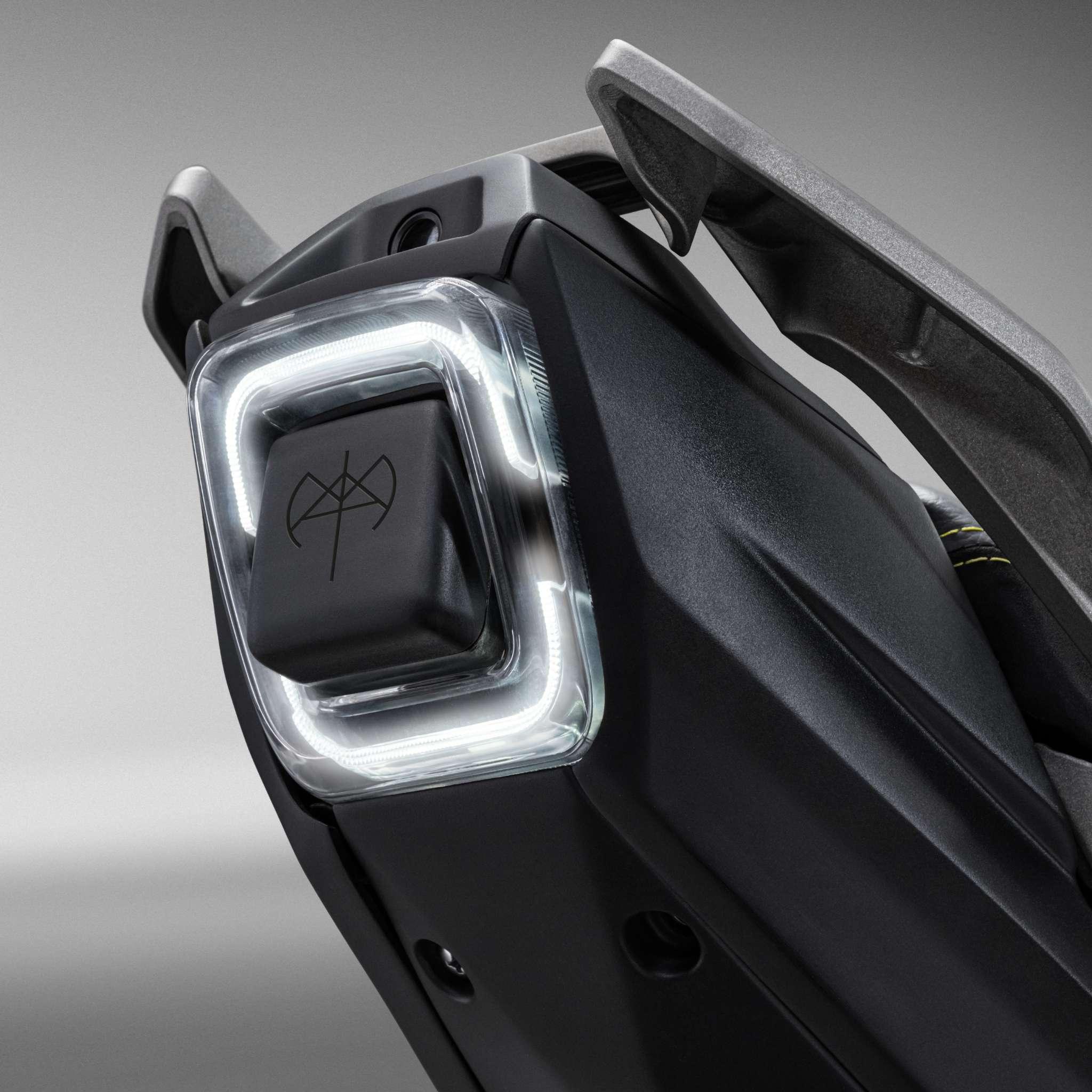 Nahaufnahme des kantigen schwarzen NAXEON E-Motorrad I AM. PRO-Gerätes mit einer leuchtenden, quadratischen LED-Taste und einem abstrakten "N"-Emblem. Das vom Turbo Boost inspirierte Design hebt sich von dem unscharfen grauen Hintergrund ab.