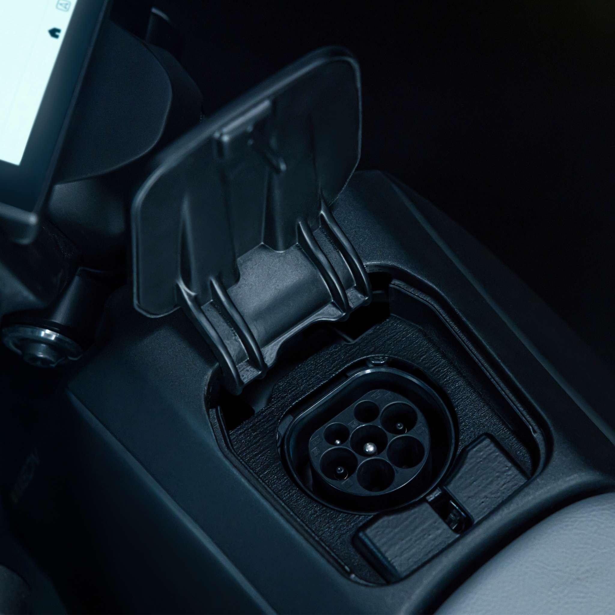 Nahaufnahme der geöffneten Abdeckung des Ladeanschlusses im Inneren eines NAXEON E-Motorrad Naxeon I AM. PRO (Kopie), die den Blick auf die elektrische Ladebuchse freigibt. Der Bereich ist dunkel, links ist ein Teil eines Bildschirms zu sehen.