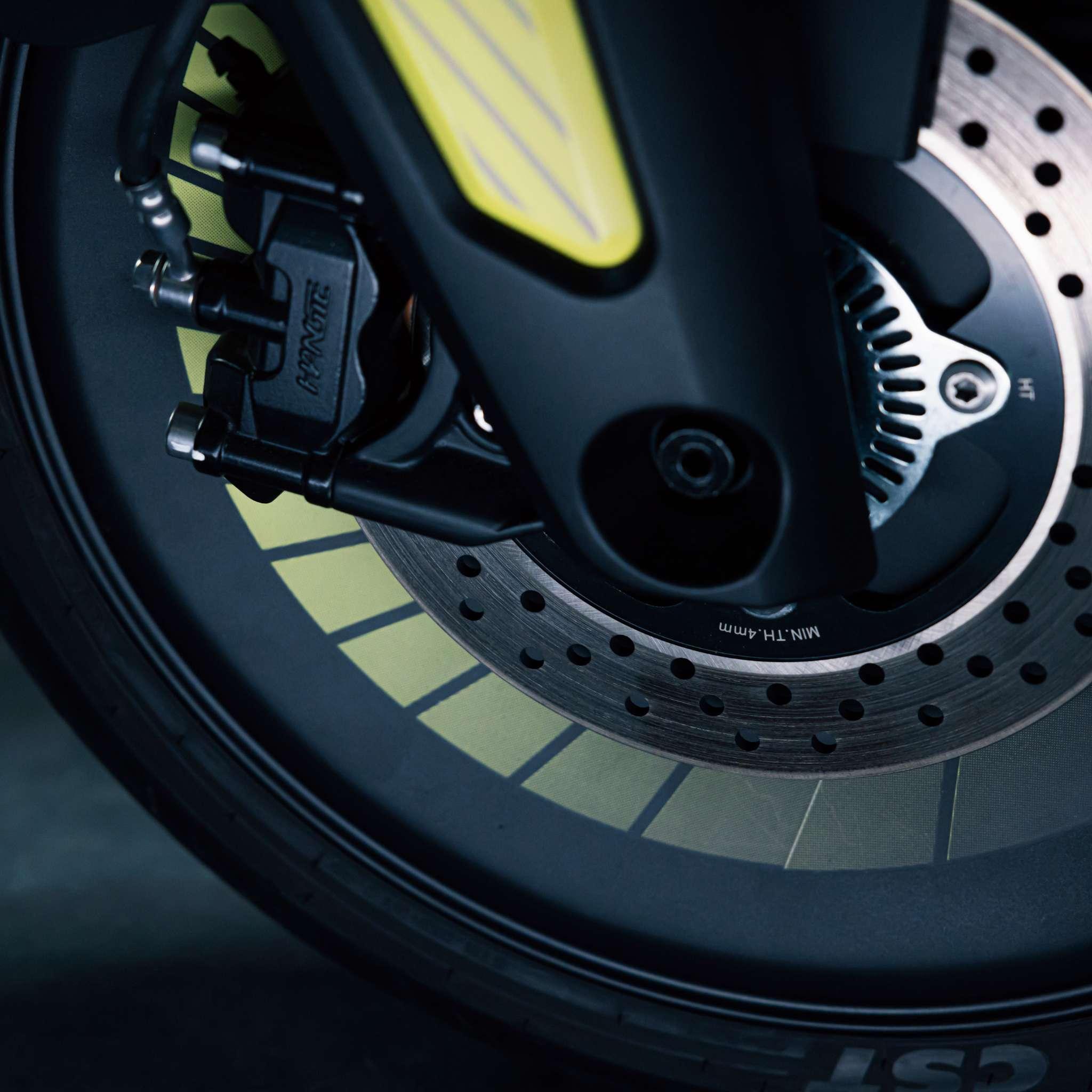 Nahaufnahme eines E-Motorrad Naxeon I AM. PRO-Rad von NAXEON. Hervorzuheben sind die gelochte Bremsscheibe, der Bremssattel, die Federgabel und das sichtbare Reifenprofil mit auffälligen gelben und schwarzen Details für ein sportliches Aussehen.