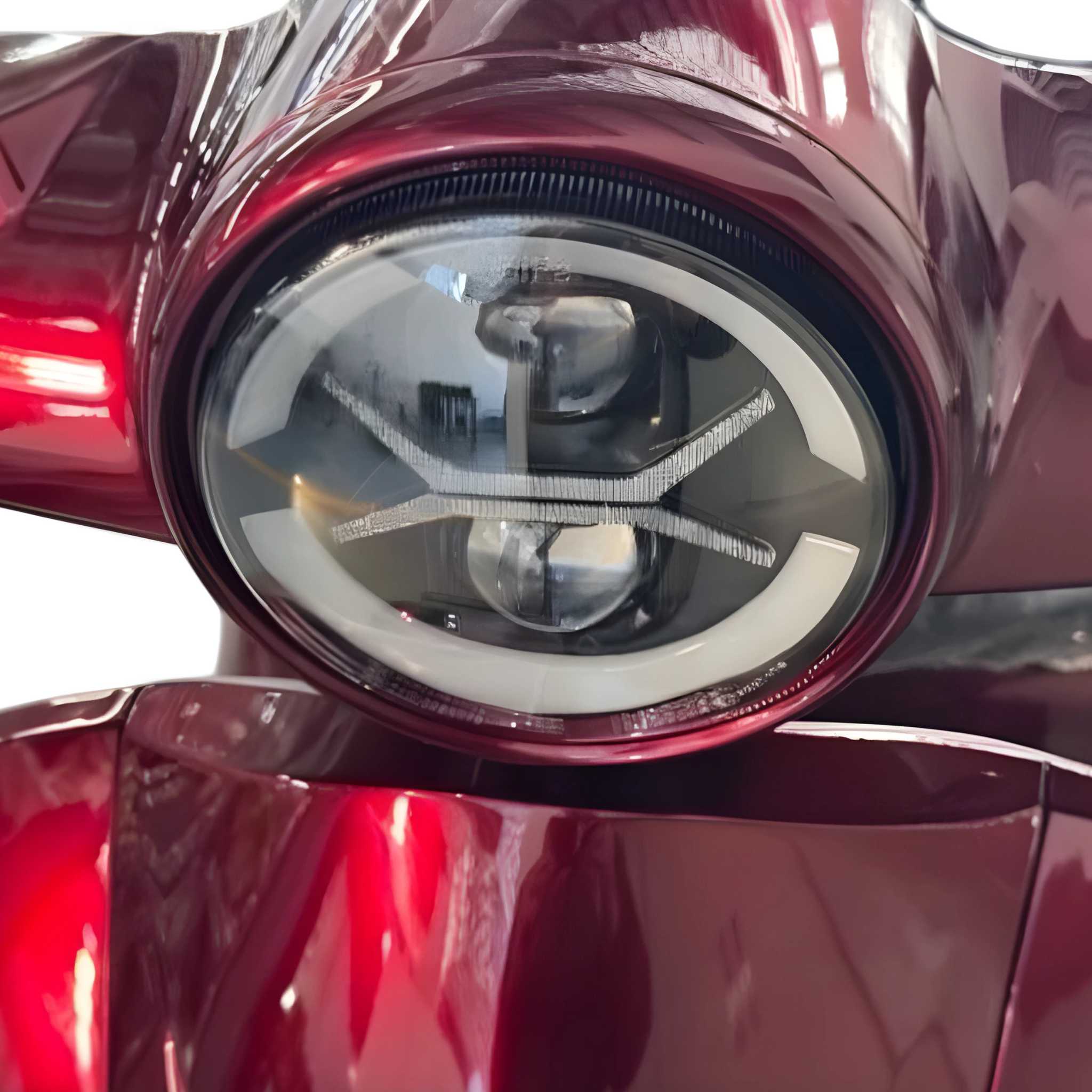 Nahaufnahme des schlanken, kreisrunden LED-Scheinwerfers am leuchtend roten Trinity ATLAS Elektromobil 4-Rad Mobilitätsroller (bis 20 km/h, bis 144 km Reichweite), der sein modernes Design und seine Eignung für tägliche Fahrten mit Straßenzulassung unterstreicht.