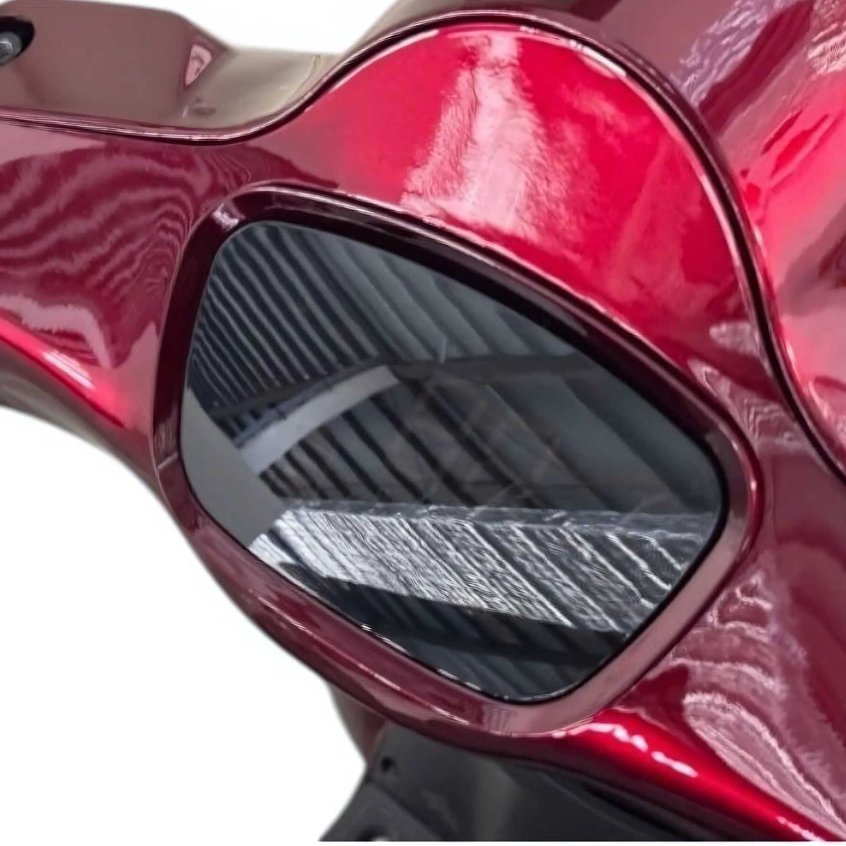 Nahaufnahme einer glänzenden, rot-metallischen Oberfläche mit einem getönten, ovalen Fenster, in dem sich Streifenmuster und die Deckenkonstruktion spiegeln– dies unterstreicht das elegante Design des Trinity ATLAS 1800 Elektromobil von Trinity, eines seniorengerechten Mobilitätsrollers mit Straßenzulassung, und verdeutlicht die fortschrittliche Entwicklung der elektrischen Mobilität mit einer Reichweite von bis zu 144 km und einer Höchstgeschwindigkeit von 20 km/h.
