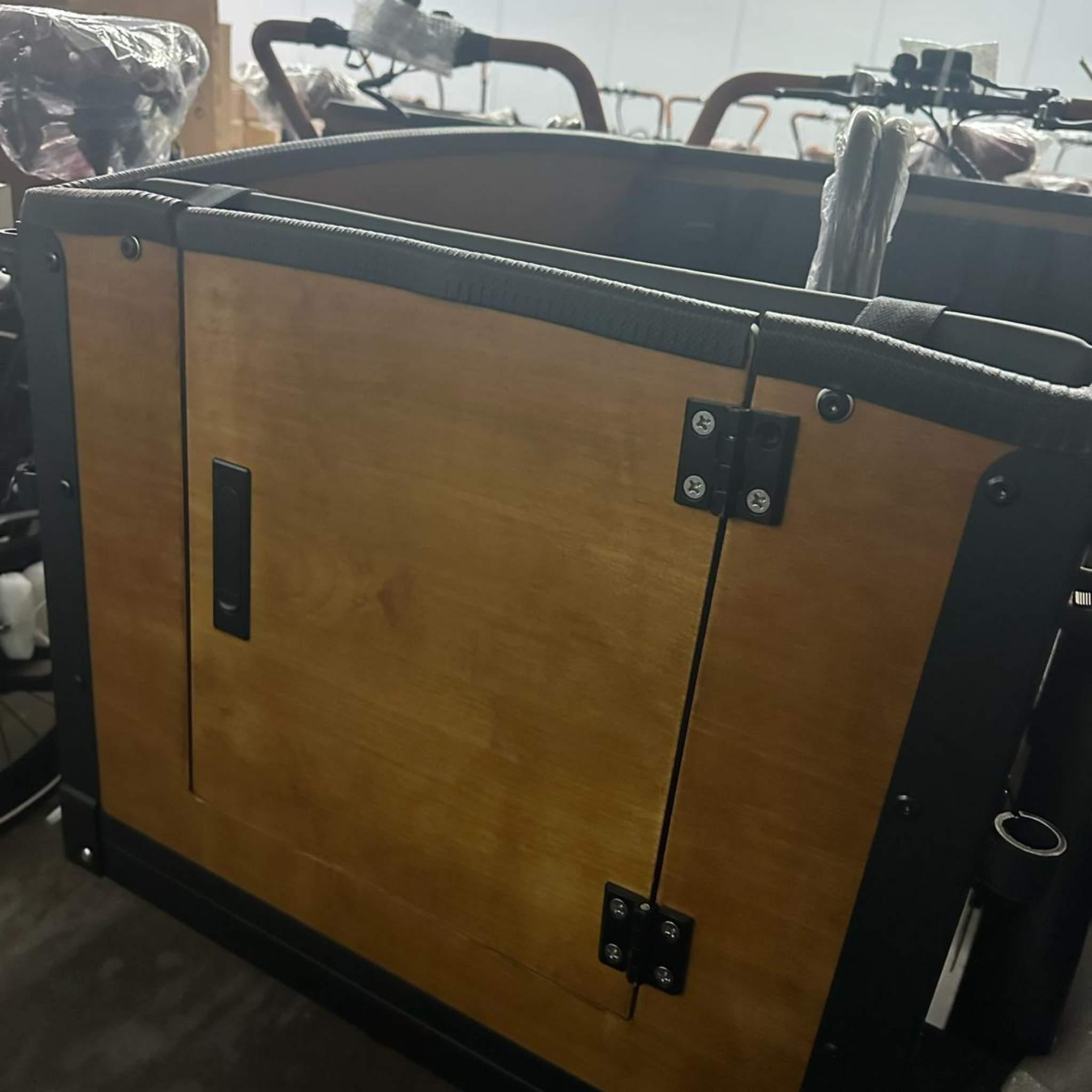 Eine Nahaufnahme einer hölzernen Ladekiste mit Flügeltür und Metallgriff, montiert auf dem Tinbot Elektro Lastenrad TB-B1 / B2 inkl. Regendach. Regendach, in einer Innenumgebung.