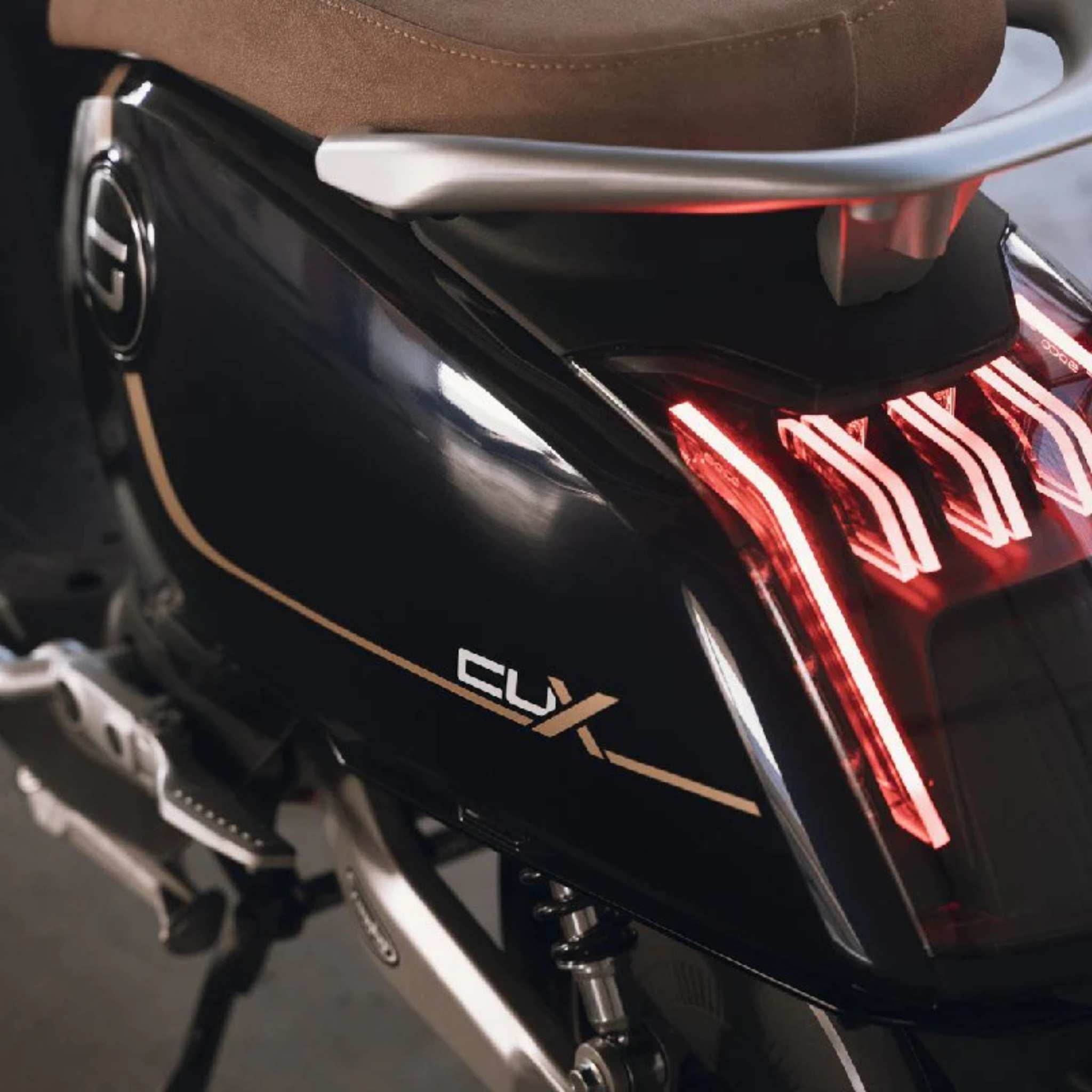 Nahaufnahme des Super Soco Elektroroller CUx Pro, die das moderne LED-Rücklicht, die schwarze Lackierung mit braunem Sitz und den goldenen Modellnamen zeigt - und den eleganten E-Scooter mit Bosch-Antrieb, der 45 km/h erreicht.