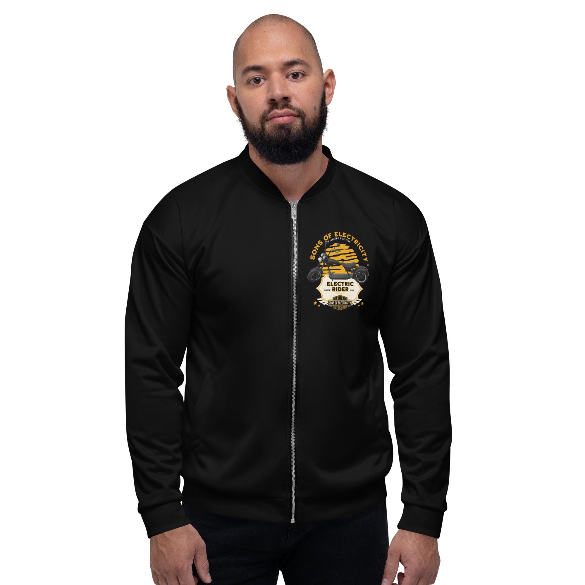 Ein bärtiger Mann trägt die SONS OF ELECTRICITY Premium E-Chopper (1) Bomberjacke: Electric Rider Limited Edition in Schwarz mit einem gelb-weißen Emblem auf der Brust. Er steht mit dem Gesicht nach vorne vor einem schlichten weißen Hintergrund.