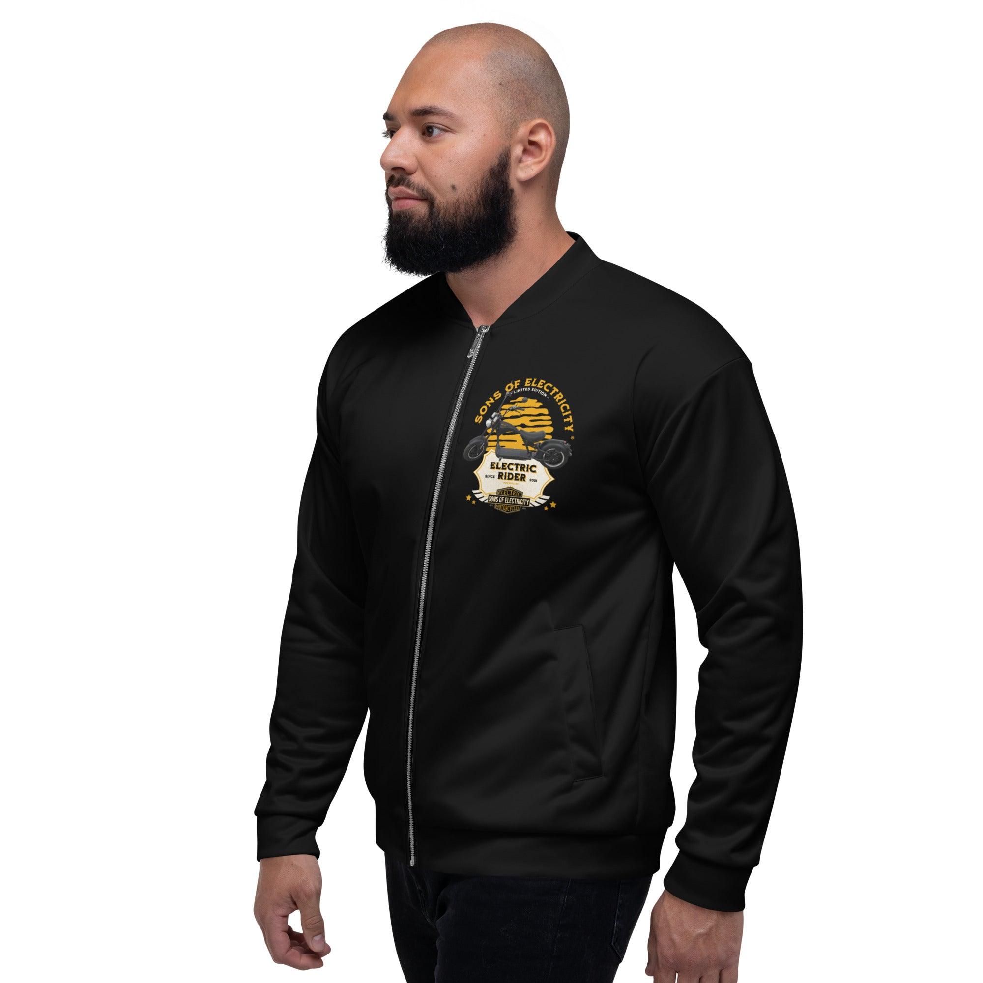 Ein bärtiger Mann trägt die SONS OF ELECTRICITY Premium E-Chopper (1) Bomberjacke, die mit einer "Born to be electrician"-Grafik mit Werkzeugen und Sternen versehen ist. Diese Electric Rider Limited Edition Jacke ist perfekt für Fans der Marke.