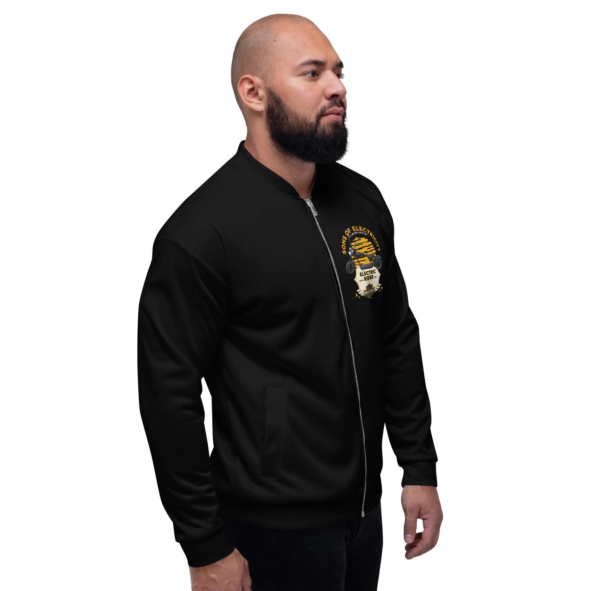 Ein bärtiger Mann in der SONS OF ELECTRICITY Premium E-Chopper (1) Bomberjacke mit gelber und weißer SONS OF ELECTRICITY-Grafik steht vor einem schlichten weißen Hintergrund und schaut leicht zur Seite.