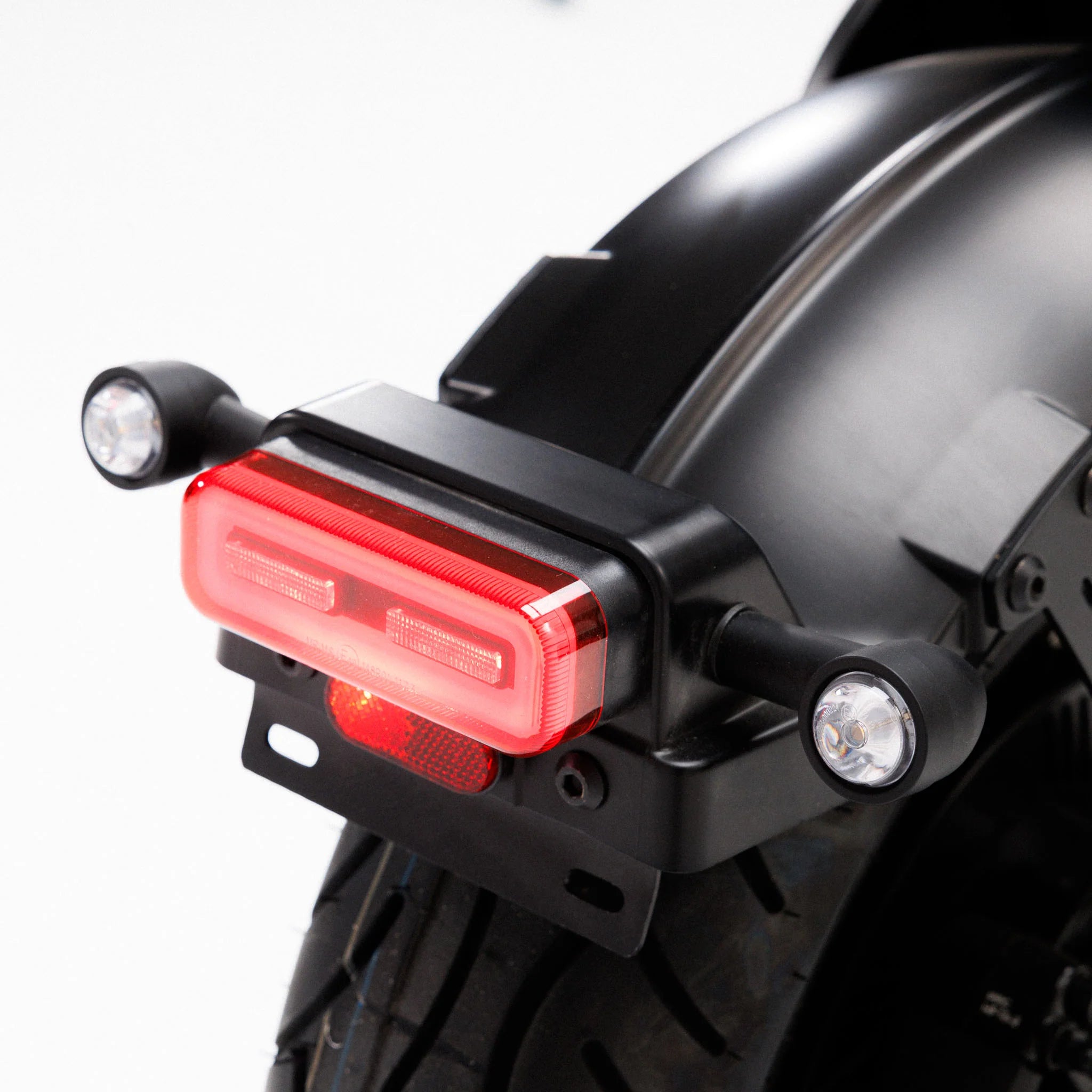 Nahaufnahme des Coopop Bobber – des leistungsstärksten E-Choppers seiner Klasse (45 km/h, L1e) – mit einem leuchtend roten LED-Rücklicht und zwei runden Blinkern auf jeder Seite des hinteren Kotflügels, wobei ein Teil des Reifens und der schwarze Rahmen zu sehen sind.