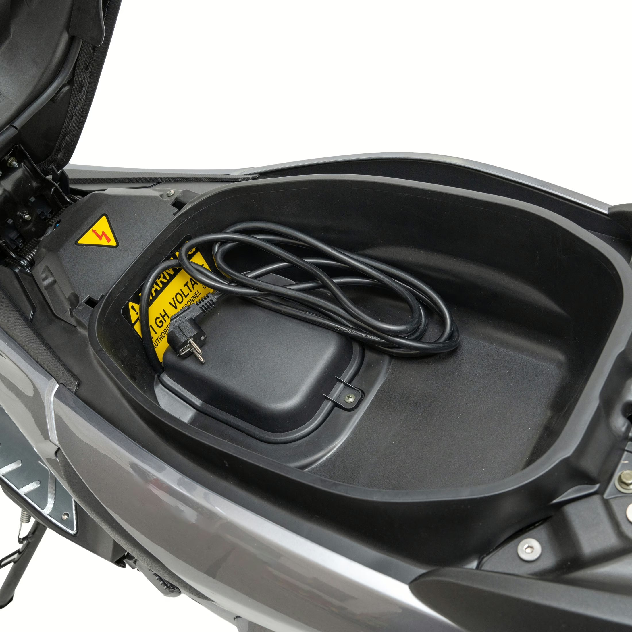 Offenes Fach unter dem Sitz eines Trinity Jupiter GT 300 Elektrorollers, in dem ein aufgerolltes Stromkabel und ein gelbes Hochspannungs-Warnschild zu sehen sind.