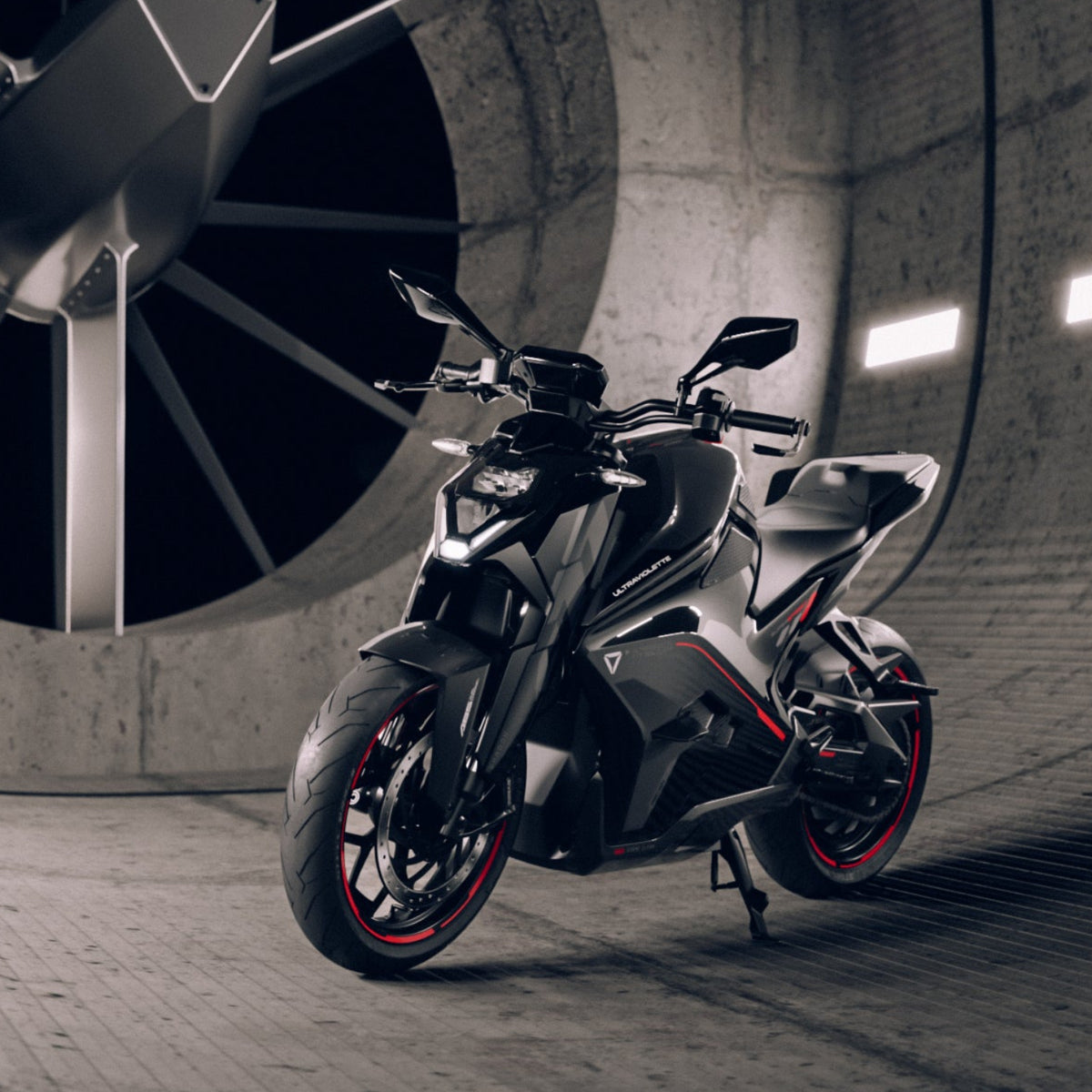 Das Ultraviolette F77 Superstreet Recon - Sportliches Elektromotorrad von Ultraviolette, in schlichtem Schwarz mit roten Akzenten, steht in einem futuristischen Windkanal mit großem kreisrunden Ventilator und beleuchteten Betonwänden.
