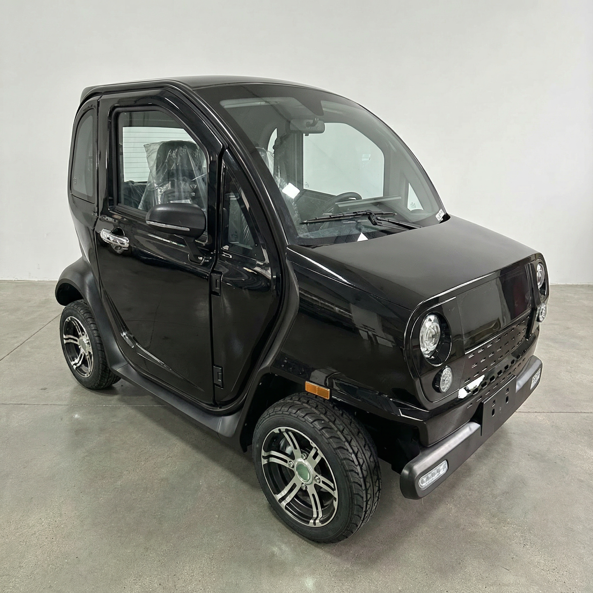 Ein schwarzer City Twister Luqi EV300 Pro Kabinenroller Facelift 2026, ein kompaktes Elektro-Mini-Auto (45 km/h), ist in einem Innenraum auf einem Betonboden geparkt. Dieses moderne, minimalistische Mikroauto hat abgerundete Kanten und kompakte Räder.