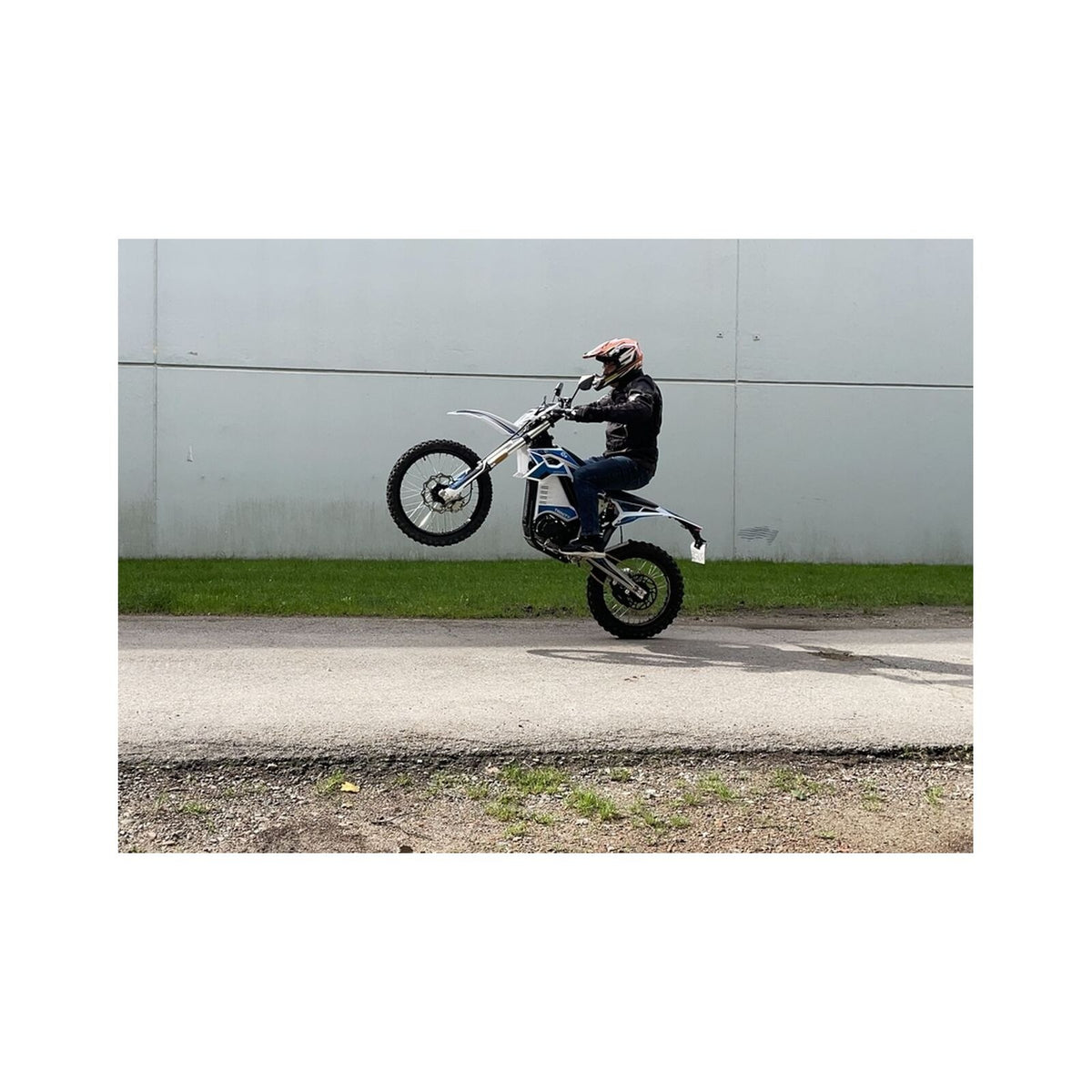 Eine Person in Motorradbekleidung führt auf einem asphaltierten Weg einen Wheelie auf einem TRINITY Panthera II: E-Enduro – einem 125 km/h schnellen Elektro-Enduro-Motorrad mit 4 Gängen – durch.