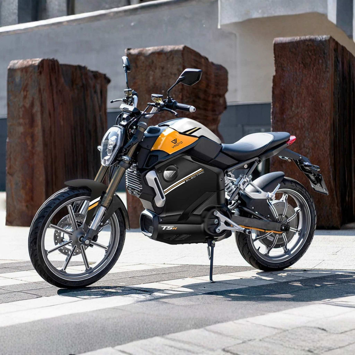 Der leistungsstarke VMOTO TSX 72V Elektroroller im Motorrad-Design steht auf einem modernen Stadt-Bürgersteig, umgeben von großen rostigen Metallskulpturen und zeitgenössischen Gebäuden.