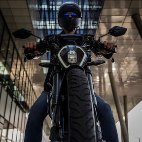 Ein behelmter Fahrer sitzt auf dem VMOTO TSX 72V - einem leistungsstarken 45 km/h Elektroroller im Motorrad-Design - mit modernen Glasgebäuden und Säulen im Hintergrund, aus einem niedrigen Winkel betrachtet.