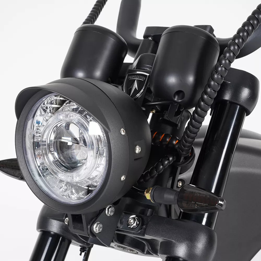 Nahaufnahme des Mangosteen MANGOSTEEN M1P Citycoco E-Choppers mit Frontscheinwerfer, Blinker, Lenker und einem Teil der Federung in schwarzem Gehäuse vor einem schlichten weißen Hintergrund.