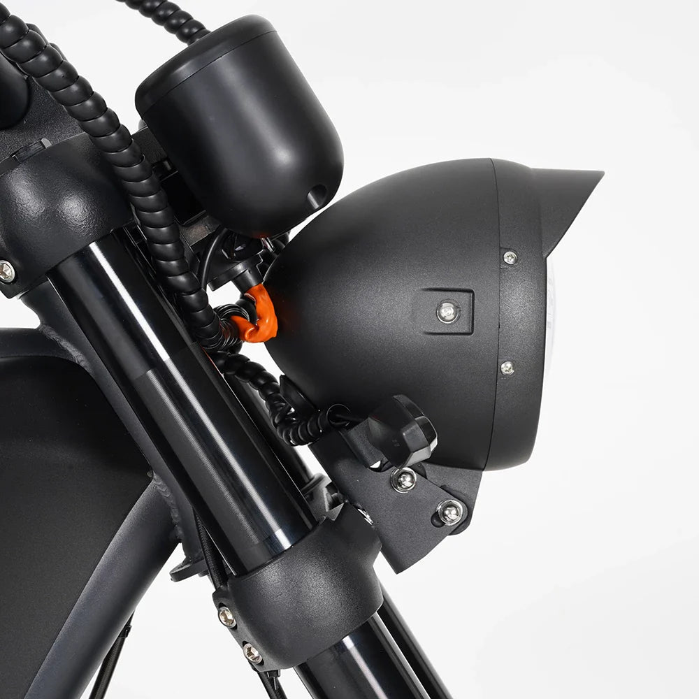 Nahaufnahme des MANGOSTEEN M1P Citycoco E-Chopper (MOD. 26) Scheinwerfers und der Vorderradgabel von Mangosteen. Hervorzuheben sind das mattschwarze Finish, die Montageteile und die Kabel vor einem weißen Hintergrund.