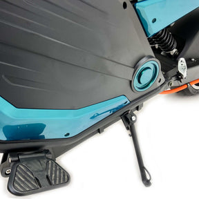 Nahaufnahme des City Twister E-Choppers Elektro Motorrad: CityTwister 6.0 PRO. Hervorzuheben sind die teal-schwarze Karosserie, die robuste Fußstütze, der Ständer und die Federung - angetrieben von einem 5000-W-Motor mit 110 km/h Höchstgeschwindigkeit - vor einem weißen Hintergrund.