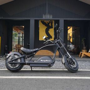 Ein stilvoller schwarzer Mangosteen E-Chopper (M1PS, 85 km/h, 40-Ah-Lithium-Akku von Samsung, 4000 Watt) steht auf einer Straße vor einem modernen Gebäude mit großen Fenstern, in dessen Inneren sich ein gelbes Kunstwerk befindet.