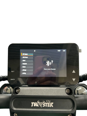 Nahaufnahme des E-Choppers: Das Armaturenbrett des CityTwister 3.0 mit dem neuen TFT-Multimedia-Spiegel-Display und einer Aufforderung zur Bluetooth-Verbindung. Auf der Lenkerhalterung ist das „City Twister“-Logo zu sehen, das das moderne Design dieses originellen Elektroroller-Modells unterstreicht. Der Hintergrund ist schlicht weiß.