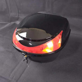 Ein kompaktes, glänzend schwarzes Topcase für den E-Scooter WANDLER-K/E von Wandler mit einem roten Reflexstreifen und einem sicheren Schlüsselschloss an der Vorderseite liegt auf einer dunklen Stoffunterlage. Dieses stilvolle und praktische Accessoire eignet sich perfekt zur Befestigung an Ihrem Gepäckträger und sorgt dafür, dass Ihre Sachen sicher und geschützt sind.