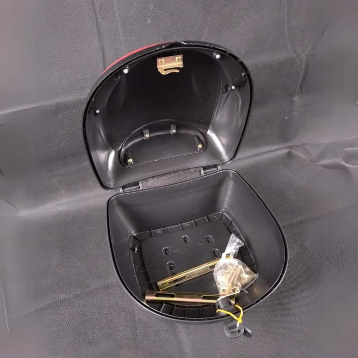 Offenes Staufach am Roller, in dem sich ein kleines Säckchen mit Schrauben, eine Metallstange und ein Schlüssel vor einem schwarzen Hintergrund im Innenraum befinden – ideal zur Aufbewahrung Ihres Wandler oder zur sicheren Befestigung von Zubehör wie dem „Topcase für E-SCOOTER WANDLER-K/E“ von Wandler oder einem Gepäckträger.
