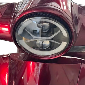 Nahaufnahme eines runden, modernen Scheinwerfers am leuchtend roten Elektromobil Trinity ATLAS 1800 – dessen glänzende Oberfläche Licht und Stil widerspiegelt. Dieser vierrädrige Mobilitätsroller von Trinity verbindet elektrische Mobilität mit auffälligem Design und ist damit eine attraktive Option für alle, die ein Seniorenmobil mit Straßenzulassung, Wechselakku-Technologie und einer Reichweite von bis zu 144 km suchen.