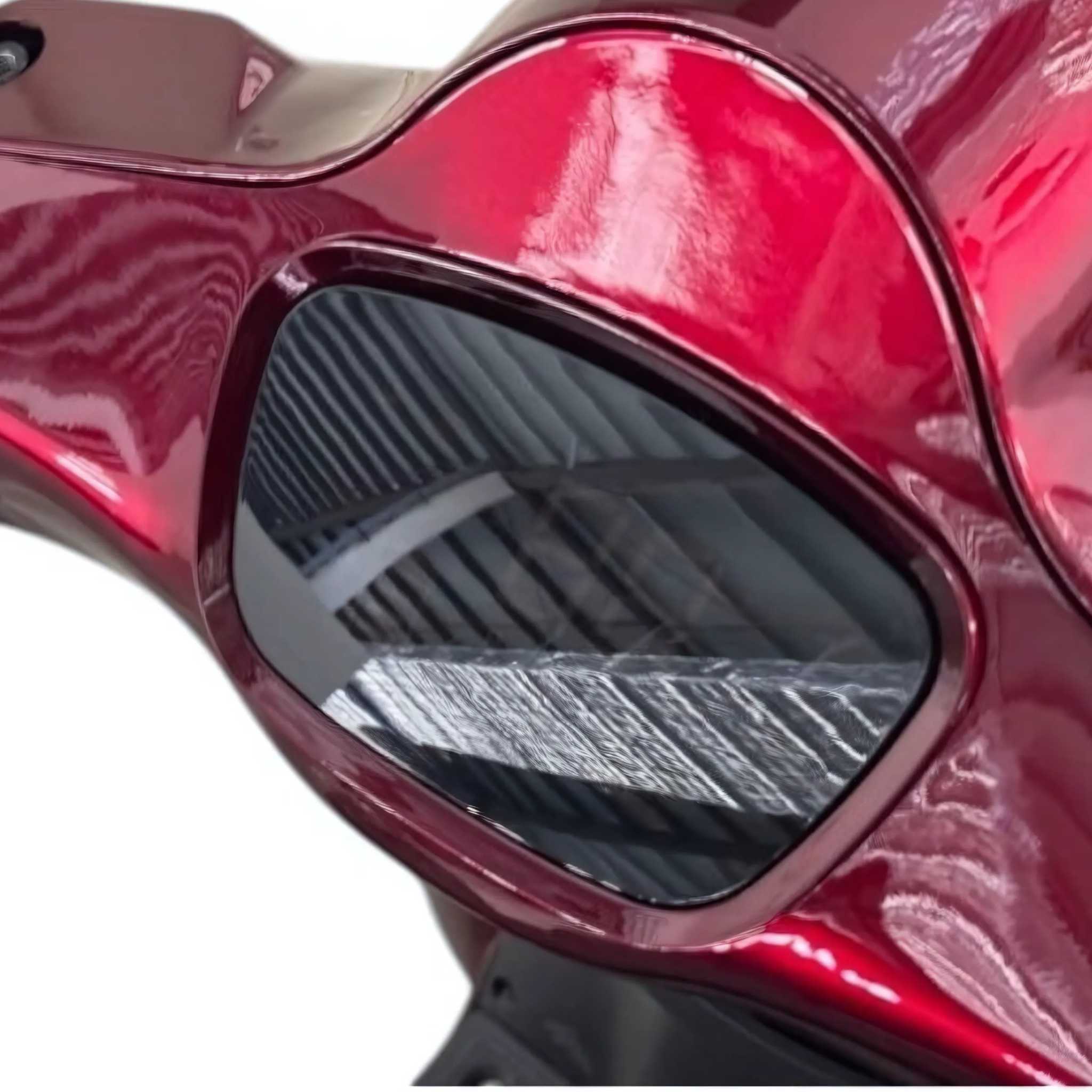 Nahaufnahme des Trinity ATLAS Elektromobils, eines leuchtend roten 4-Rad-Seniorenmobils (20 km/h) mit dunkel getöntem Visier, in dem sich die Metallbalken der umliegenden Gebäude spiegeln; zu den Merkmalen gehören Wechselakku und bis zu 144 km Reichweite.