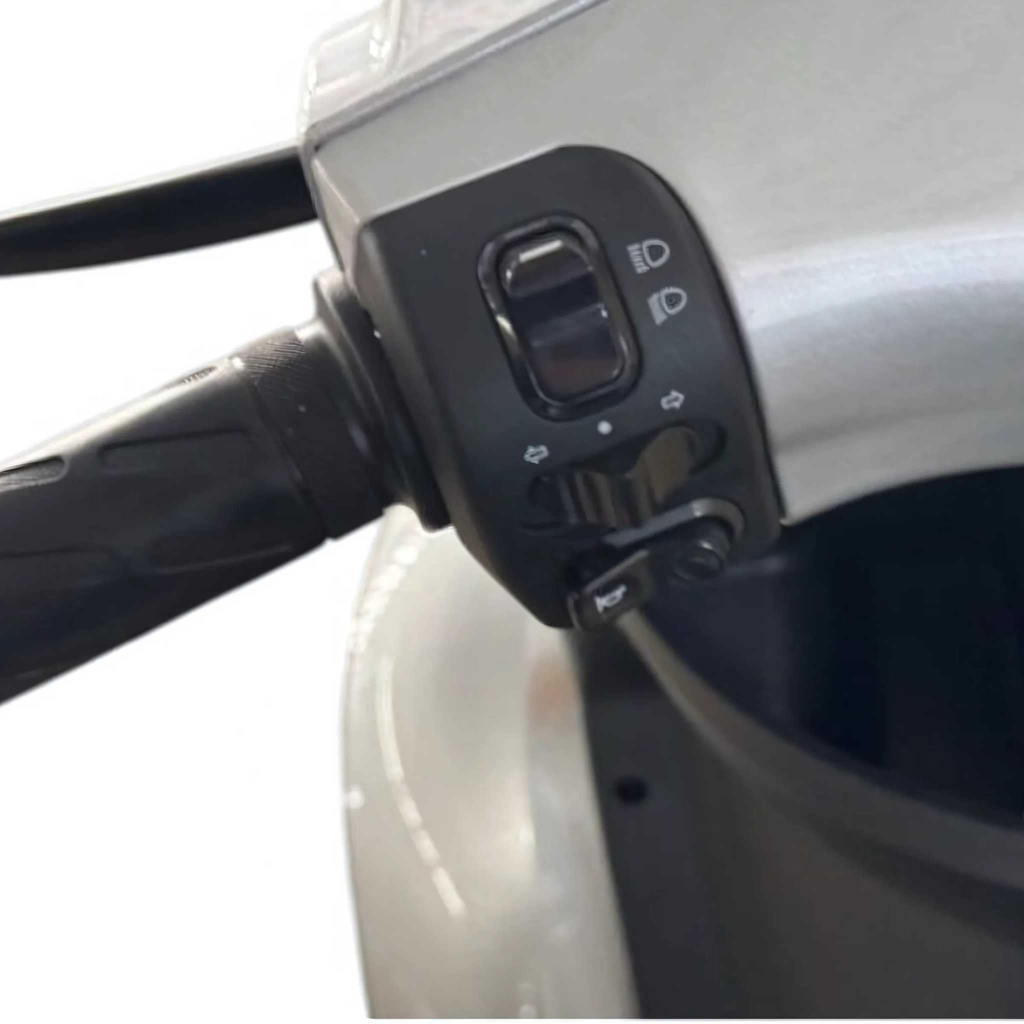 Nahaufnahme der Trinity ATLAS Elektromobil-Lenkerbedienelemente mit Schaltern für Scheinwerfer, Blinker und Hupe vor einem unscharfen Hintergrund. Seniorenmobil 20 km/h - 4-Rad, Wechselakku & bis 144 km Reichweite. Marke: Trinity.